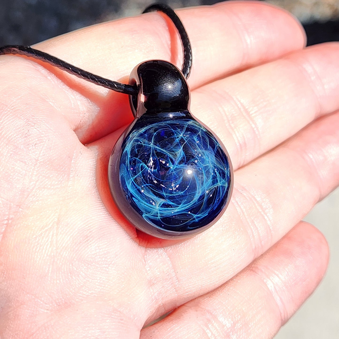 Close-up of black glass pendant with blue electric web design, handmade jewelry, on adjustable cord, gift box included