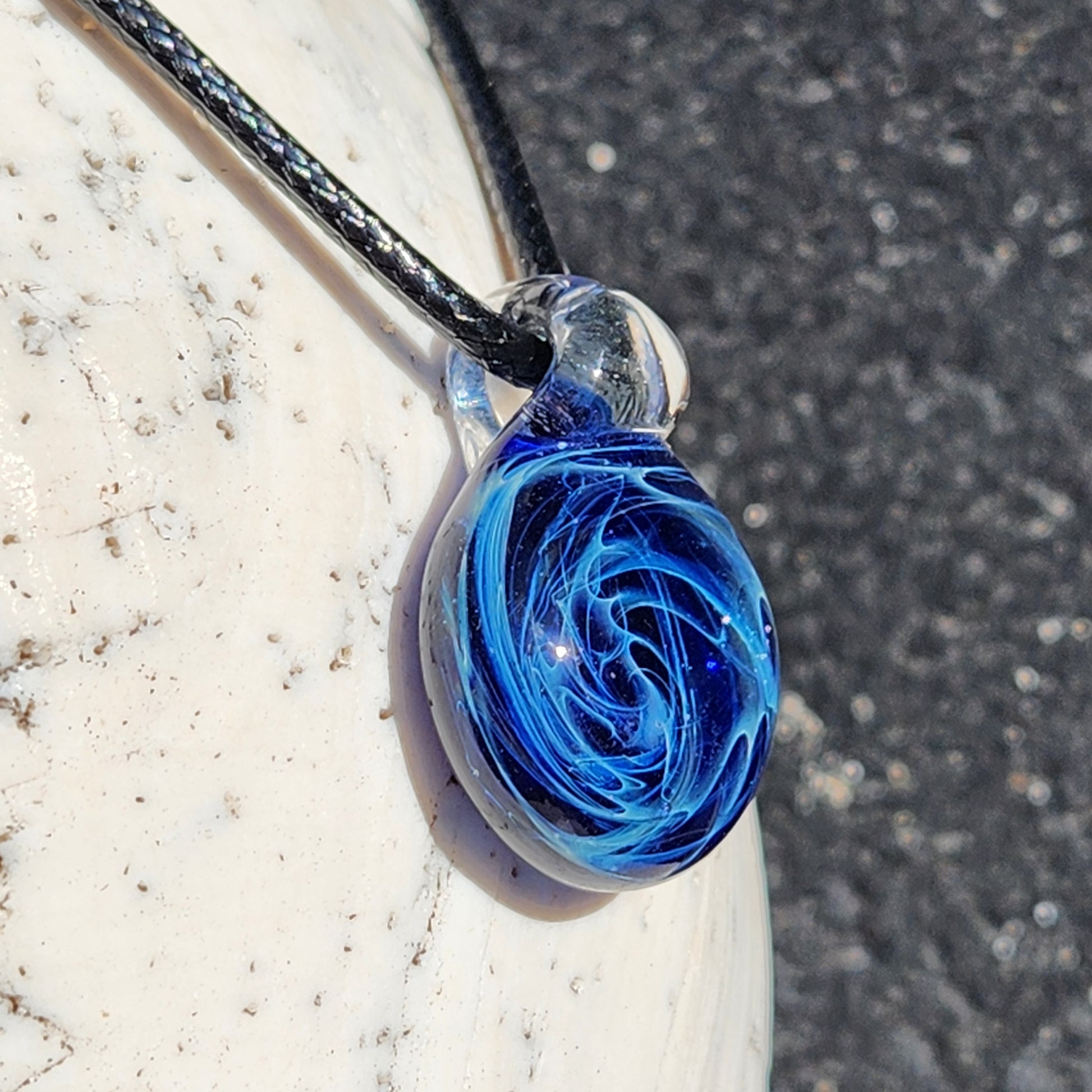 Close-up of blue glass galaxy pendant with swirling pattern, handmade jewelry, on textured surface, gift box included