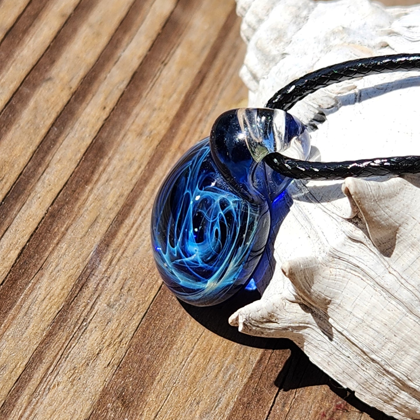 Artisan handmade blue galaxy glass pendant with swirling design, on adjustable cord, on textured surface, gift boxed