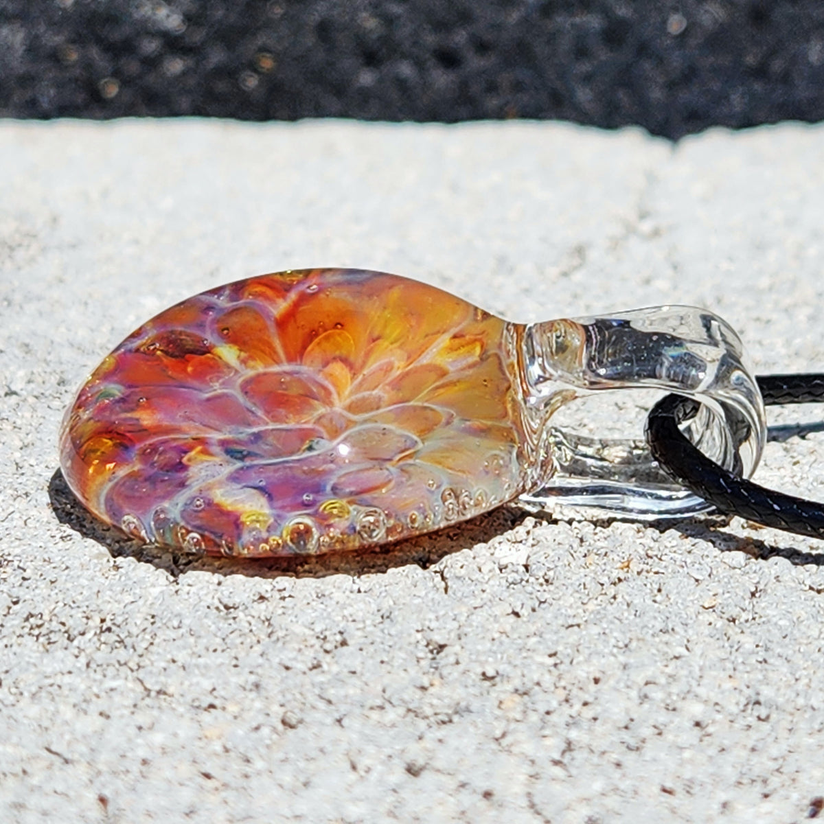 Close-up of the glass pendant showing vibrant orange, yellow, and purple colors with a glossy finish, on a black cord.