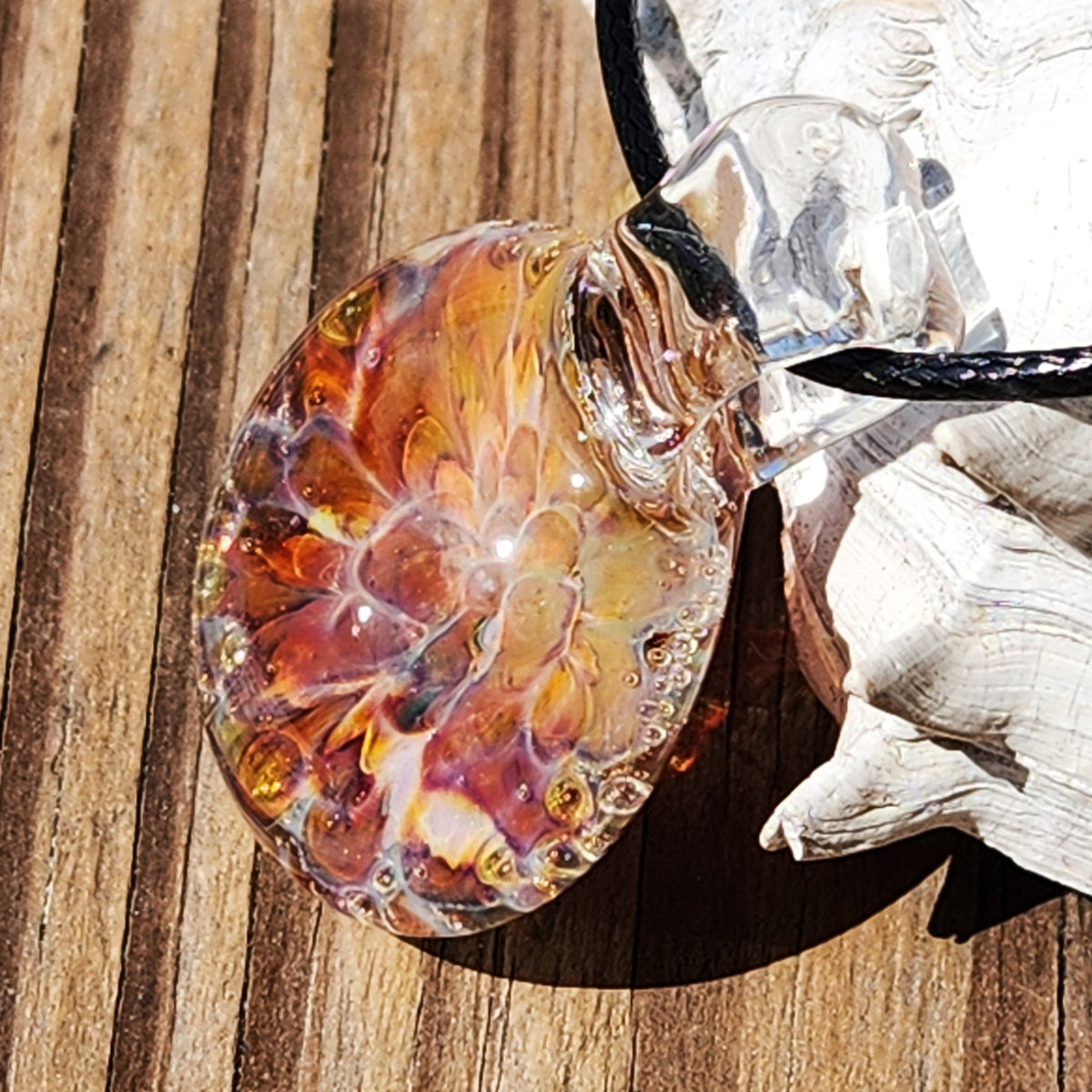 Detailed shot of the handmade sunset blown glass pendant with vivid orange and purple colors, resting on sand.