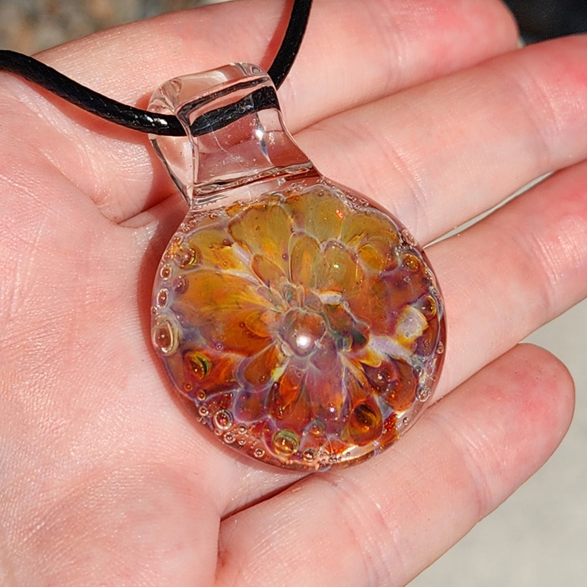 Handmade glass pendant necklace with a sunset-inspired design in warm orange, gold, and purple tones, on a black cord.
