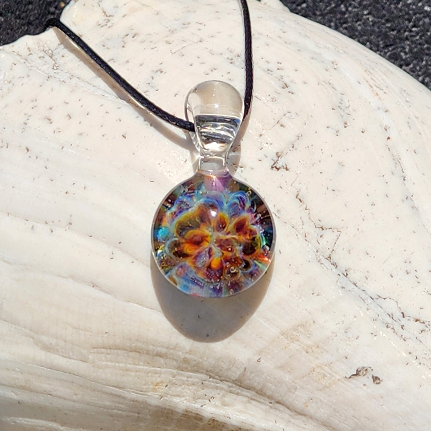Close-up of the handmade glass pendant with vibrant colors and intricate swirl design, on a white textured surface, SKU: Maly 116