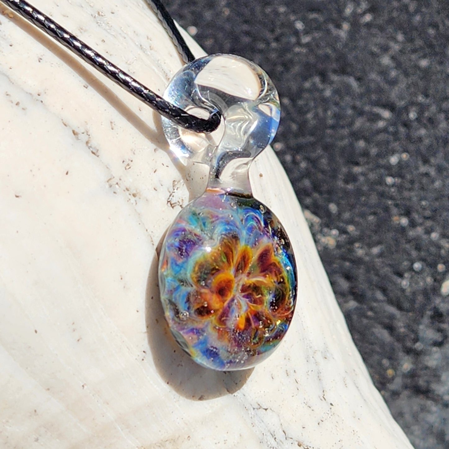 Close-up of a transparent glass pendant with a black cord, casting a shadow on a wooden surface, highlighting its glossy finish.