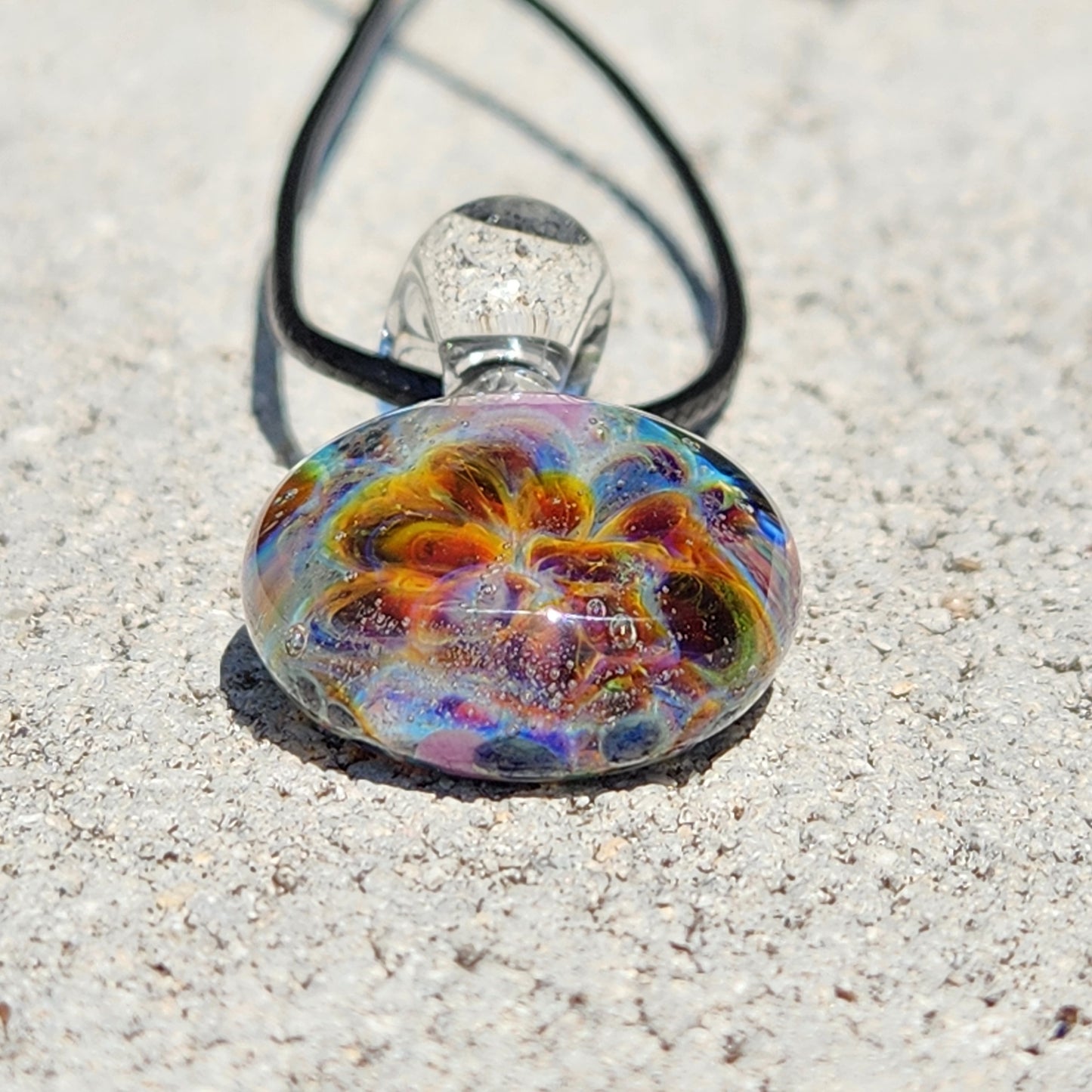 Top-down view of the multicolored glass pendant with swirling design, placed on a textured white background, SKU: Maly 116