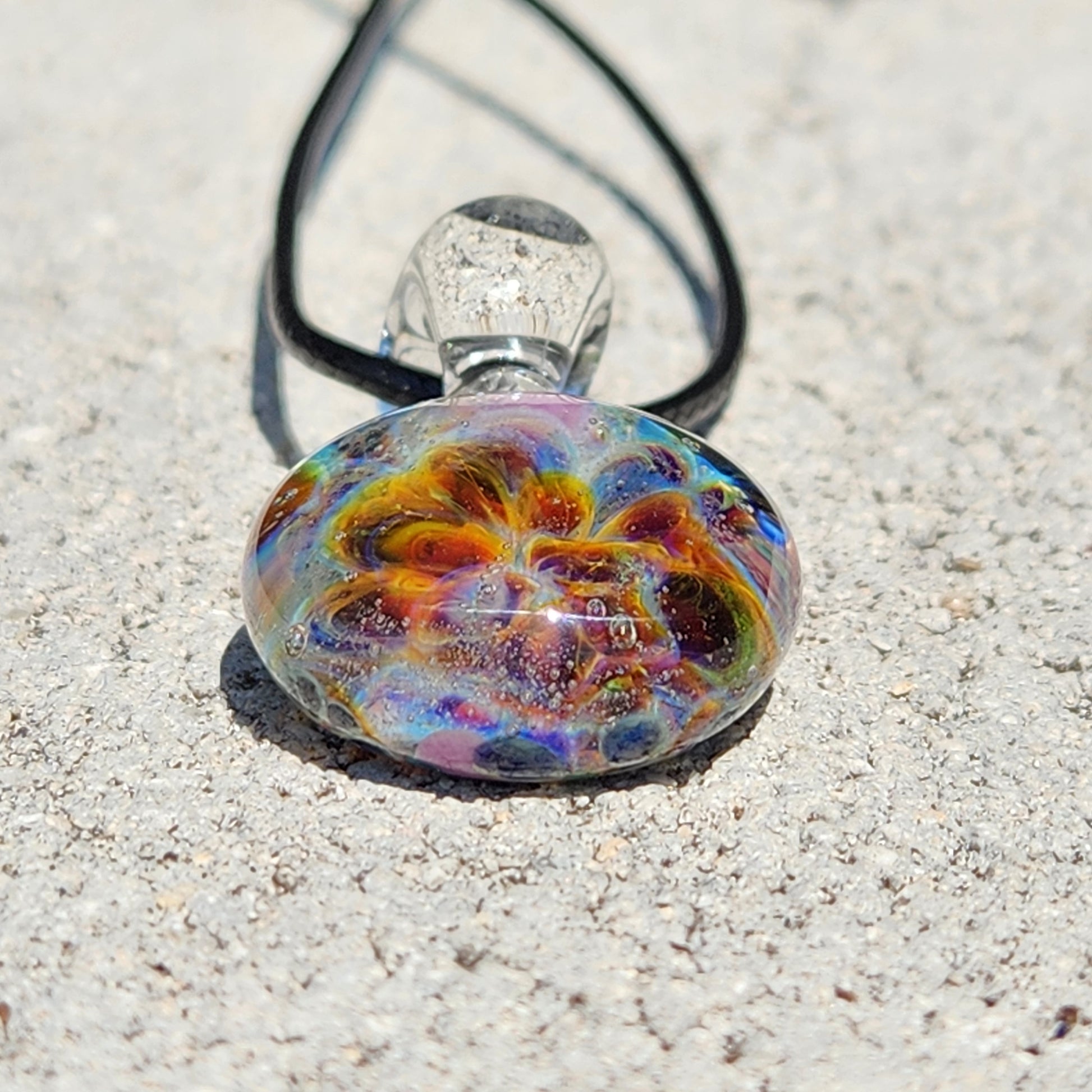 Top-down view of the multicolored glass pendant with swirling design, placed on a textured white background, SKU: Maly 116