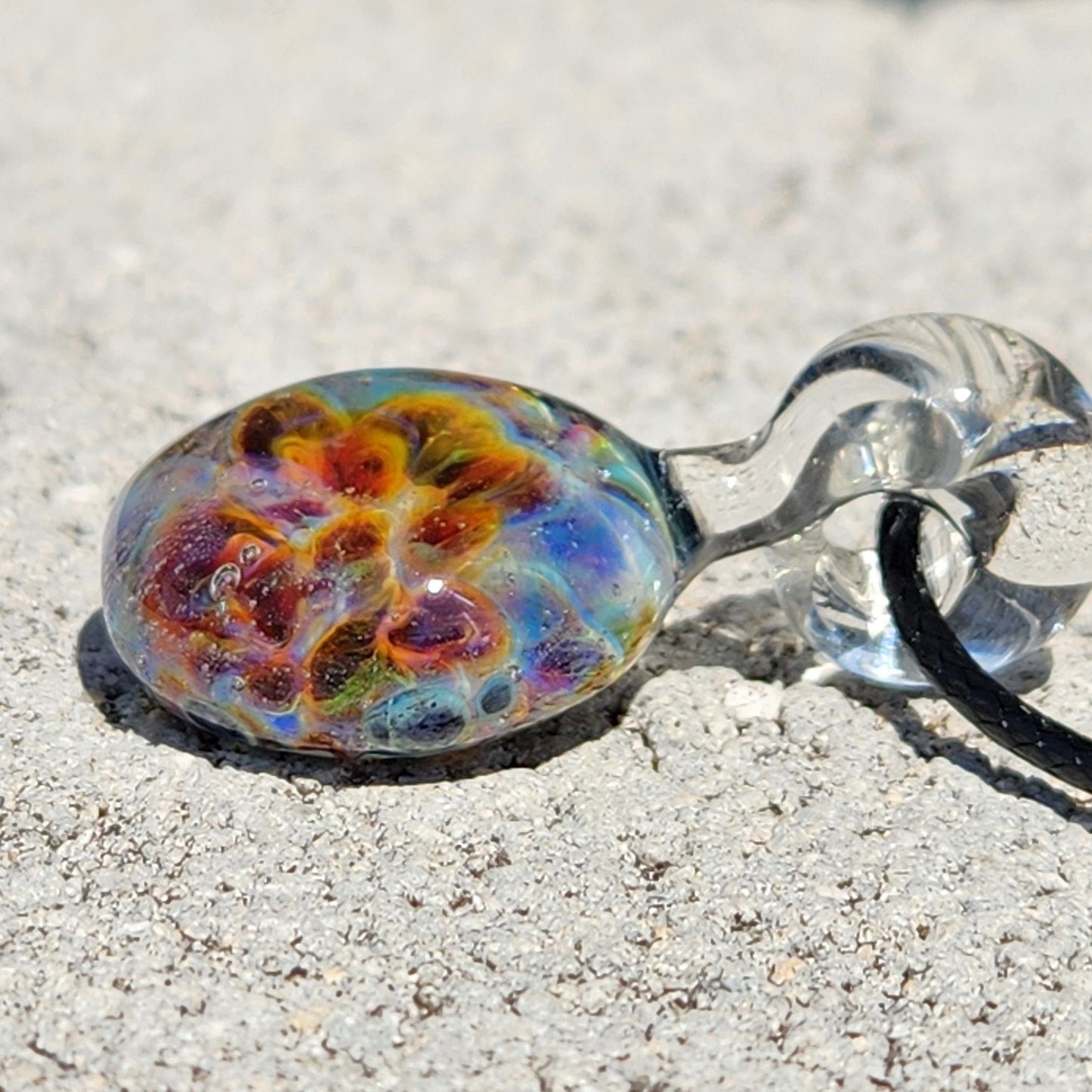 Detailed shot of a colorful glass pendant with swirling orange, yellow, and blue hues, placed on a textured wooden surface.