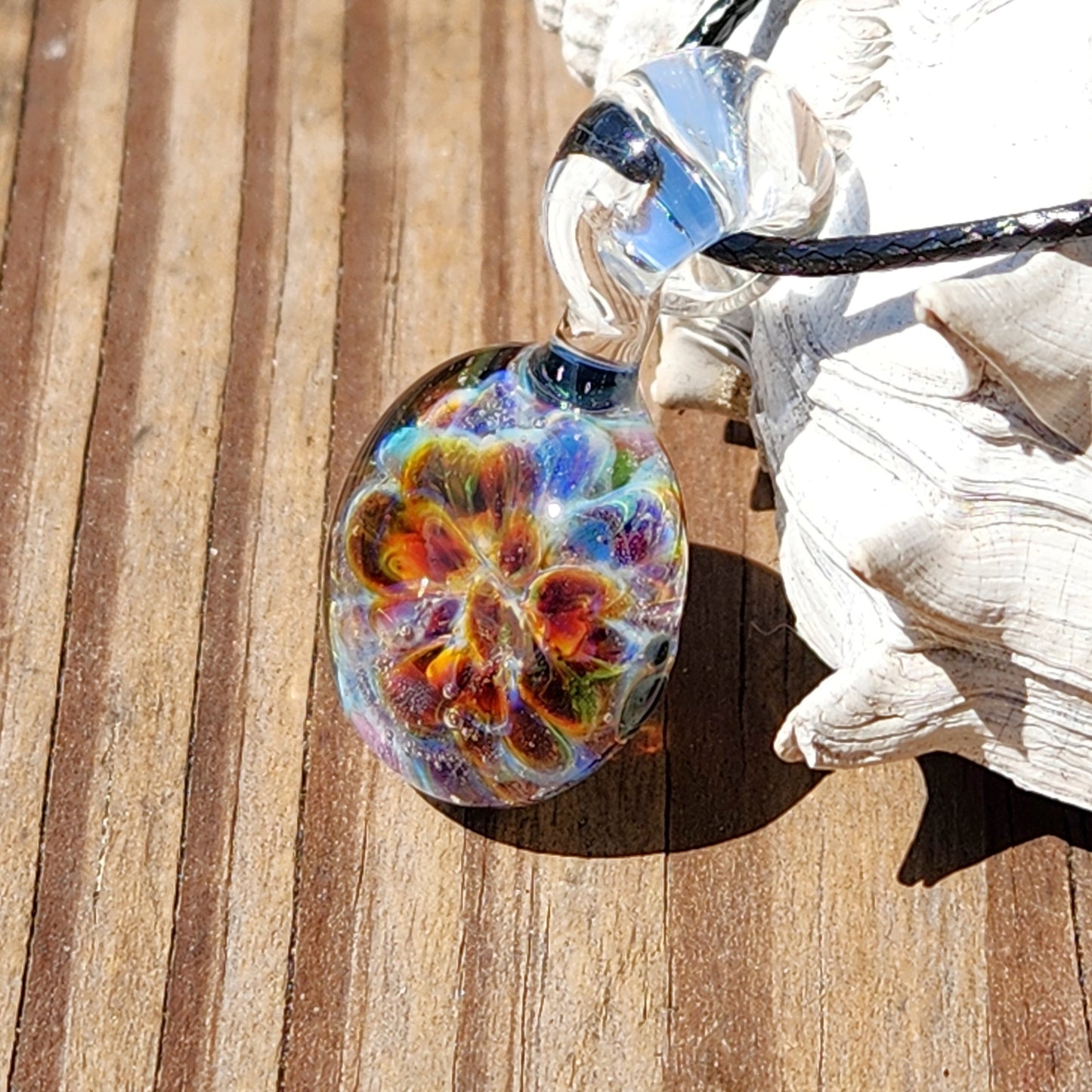 Side view of a multicolored glass pendant with intricate patterns, lying on a rustic wooden background, showcasing its detailed craftsmanship.