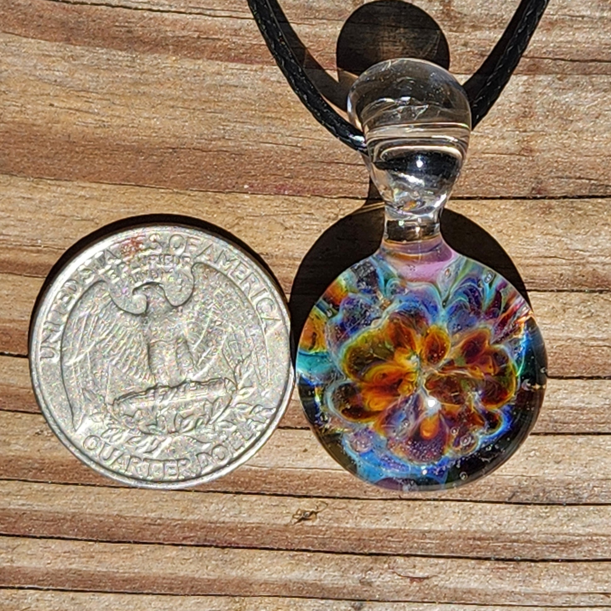 Top view of a vibrant, multicolored glass pendant with swirling patterns, resting on a wooden surface with natural light reflections.
