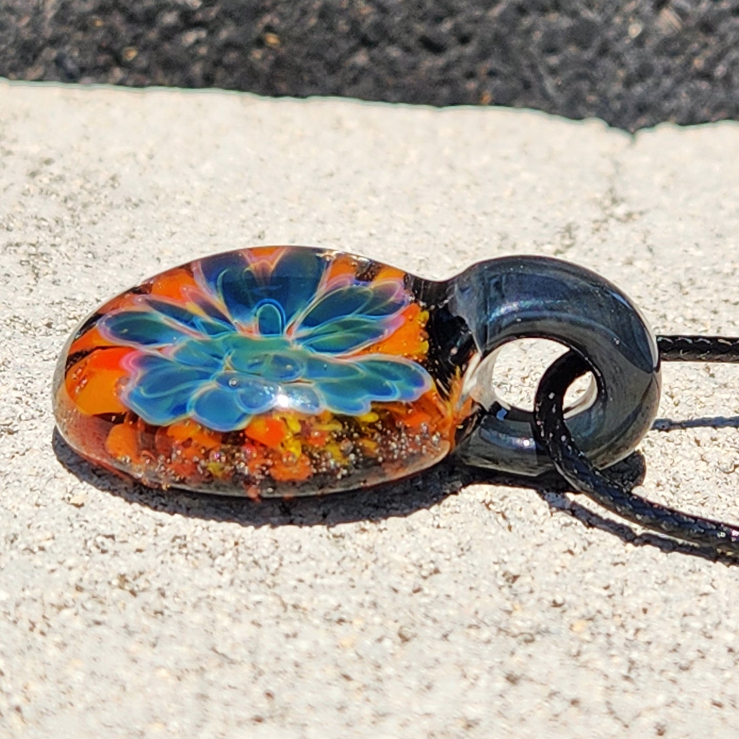 Close-up of the colorful glass pendant with a detailed blue flower and orange accents, resting on a wooden background.