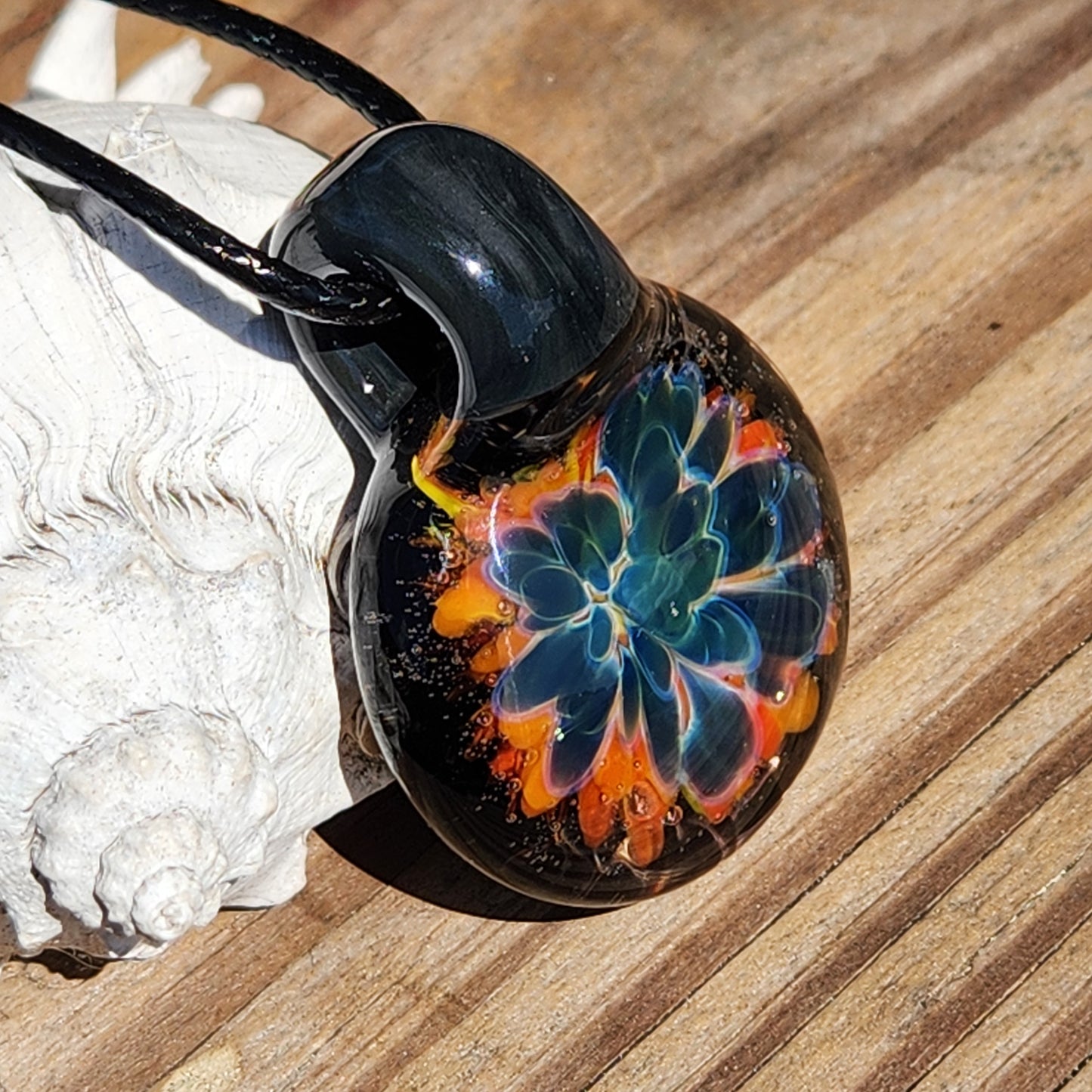 Close-up of the colorful glass pendant with a floral pattern, black cord, on a sandy background