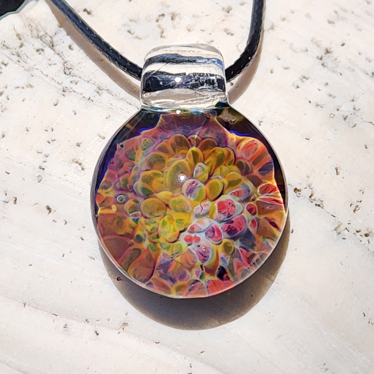 Colorful handmade glass pendant necklace with a round shape, vibrant rainbow hues, and a clear loop for wearing, crafted in the USA.