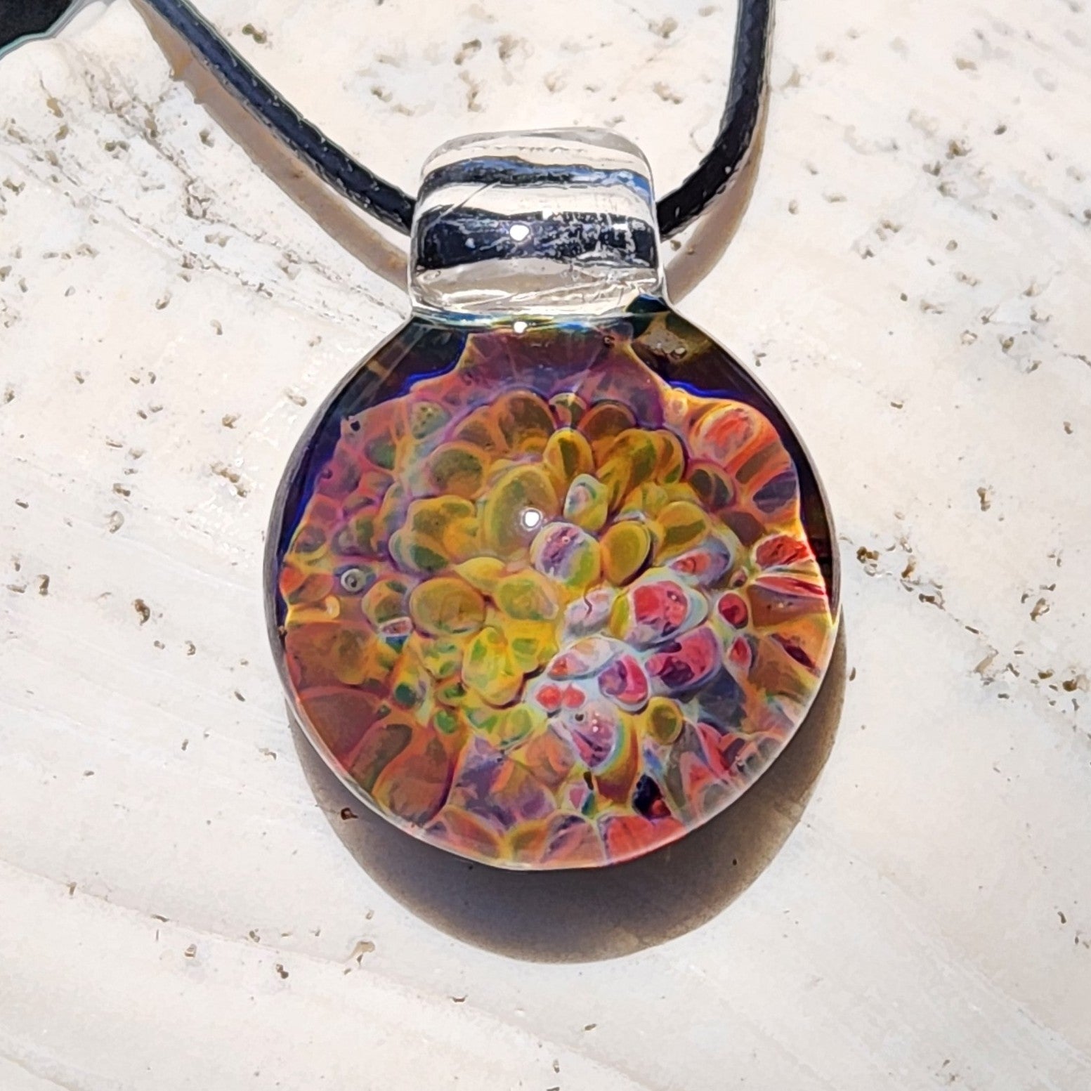 Colorful handmade glass pendant necklace with a round shape, vibrant rainbow hues, and a clear loop for wearing, crafted in the USA.