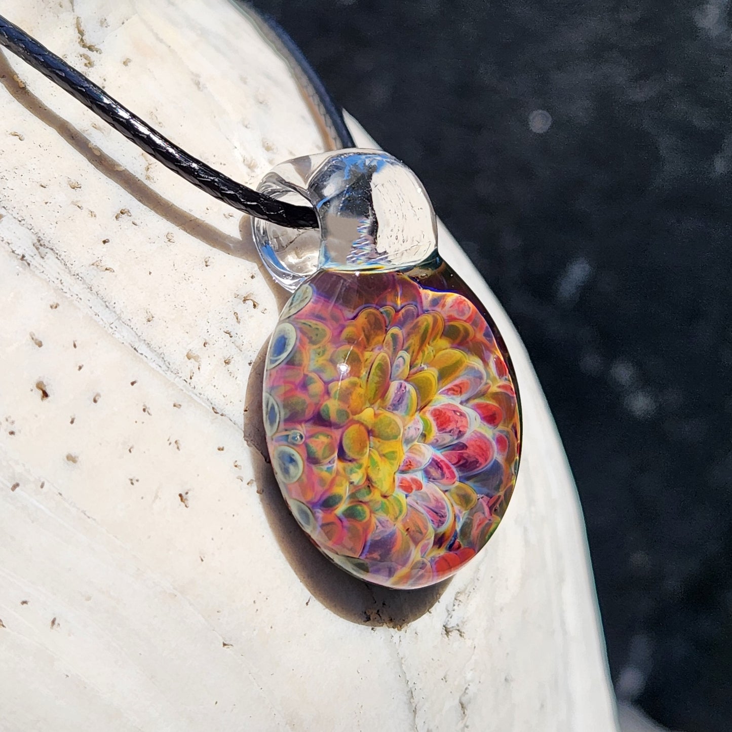Side view of the glass pendant necklace with rainbow swirl design, black cord, and clear glass loop.
