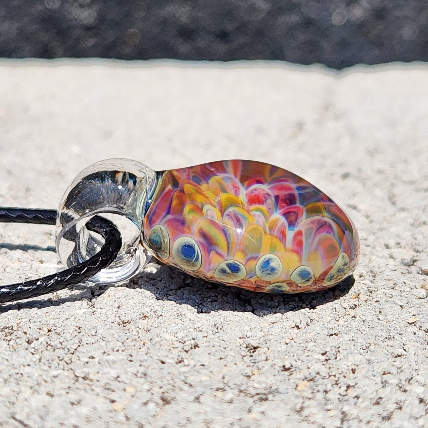 Side view of the glass pendant necklace highlighting the black cord and the detailed, colorful glass design.