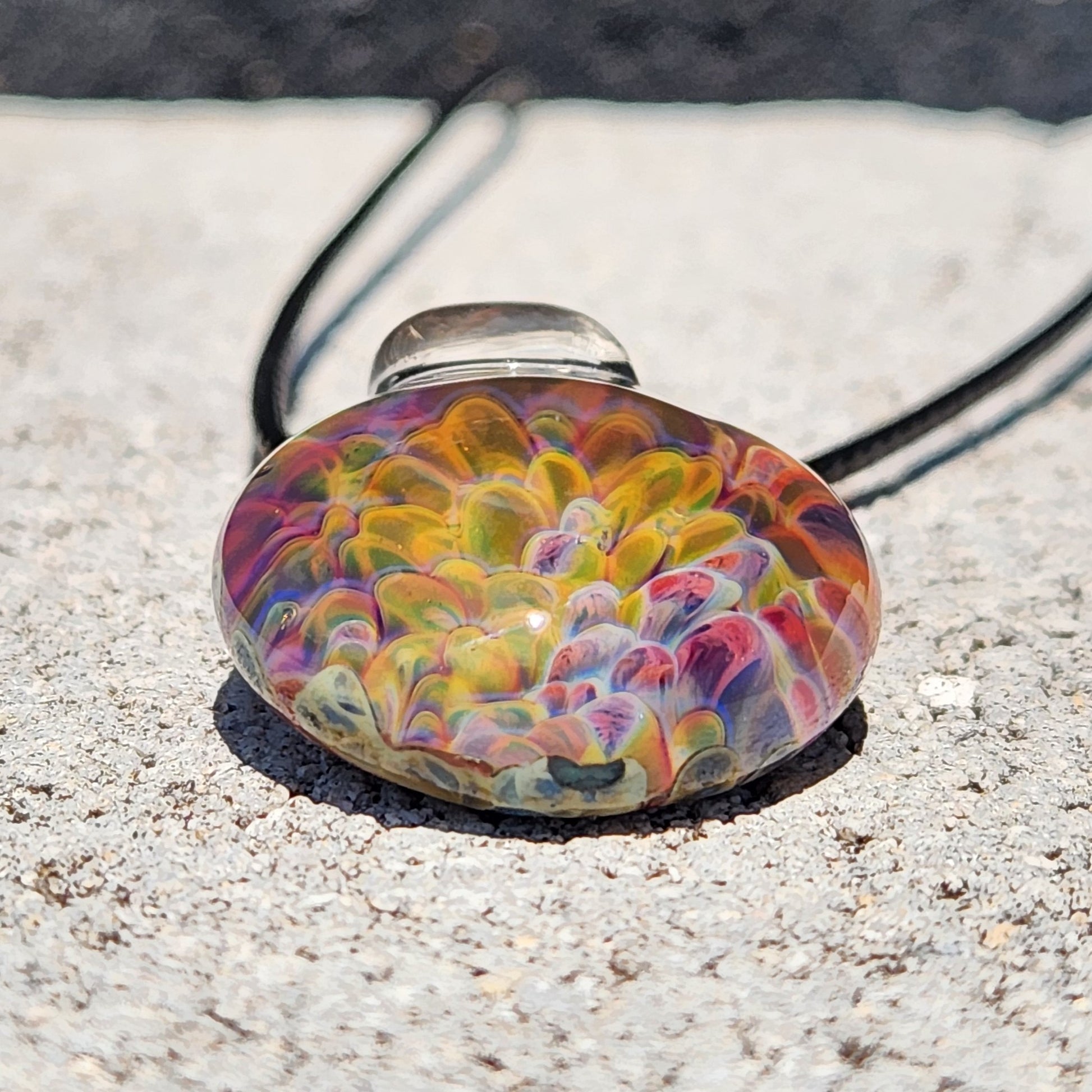Top-down view of the glass pendant necklace on a rustic wooden background, emphasizing the rainbow color pattern.