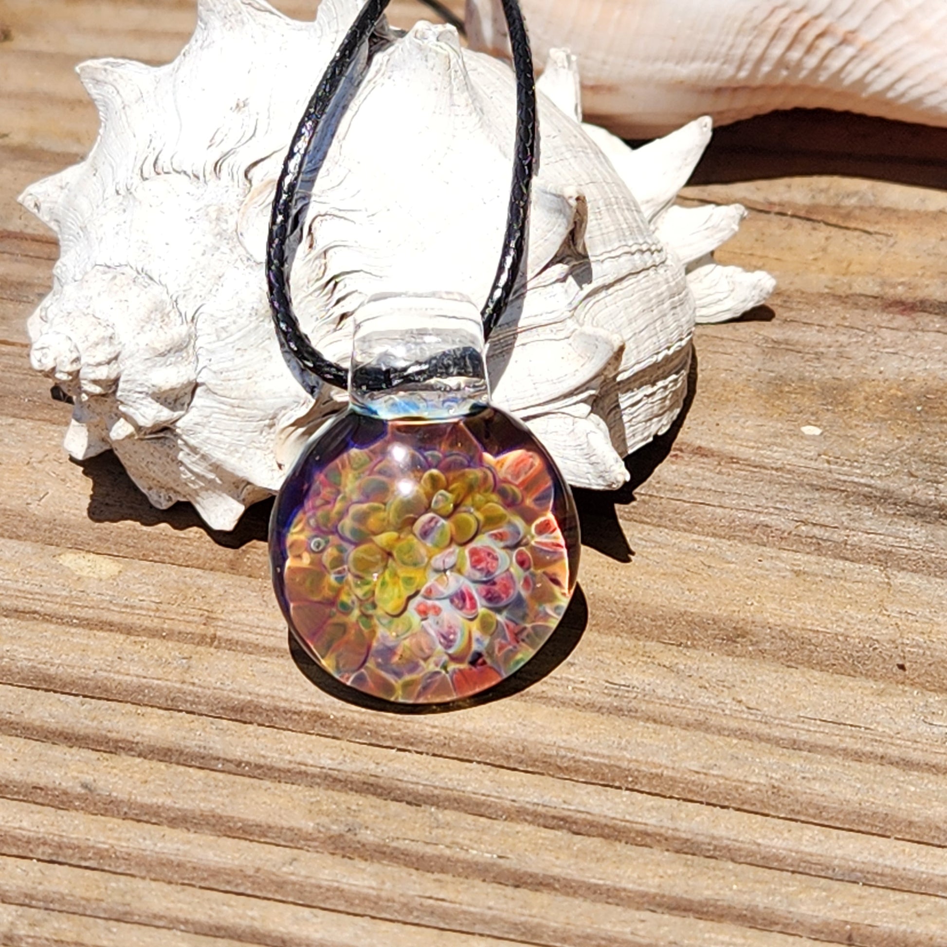 Detailed shot of the glass pendant's vibrant, swirling colors, placed on a textured wooden surface with shell accents.