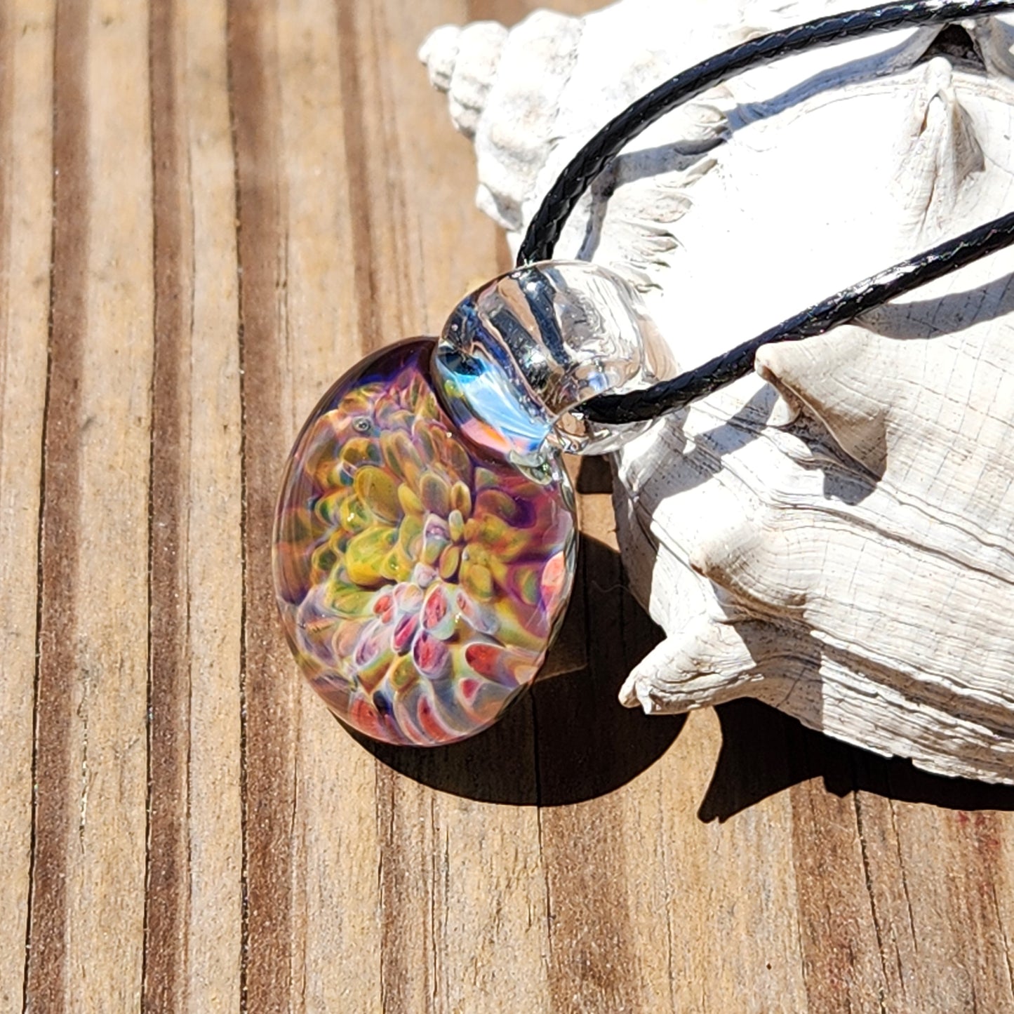 Colorful handmade glass pendant necklace with vibrant rainbow hues, clear loop, and black braided cord, crafted in the USA.