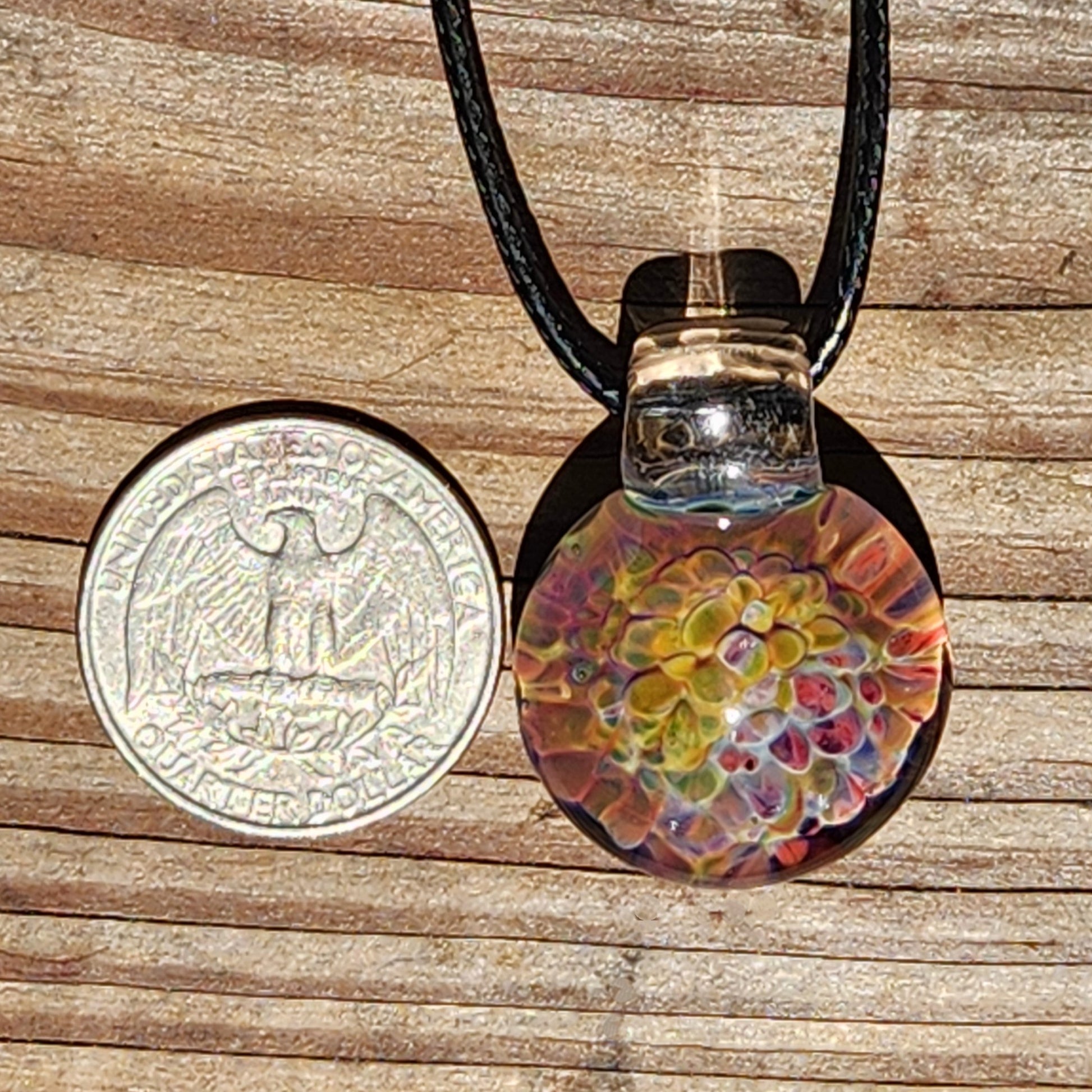 Colorful handmade glass pendant necklace with a rainbow swirl pattern, featuring vibrant hues of yellow, orange, pink, and purple, on a black cord, displayed on a wooden surface.