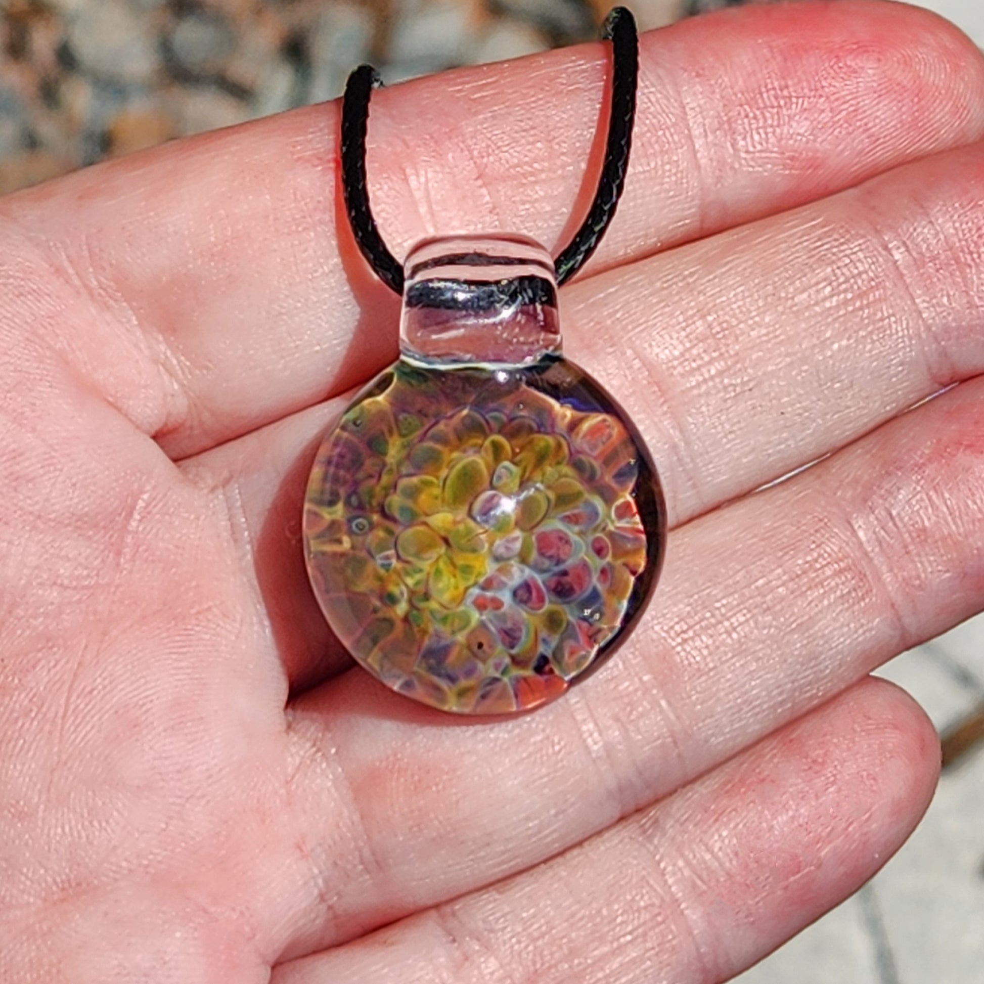 Handheld view of the glass pendant necklace with rainbow colors, black braided cord, and clear glass loop.