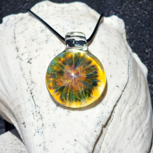 Handmade blown glass pendant necklace with vibrant multicolored swirling pattern, black cord, displayed on white shell with sandy background