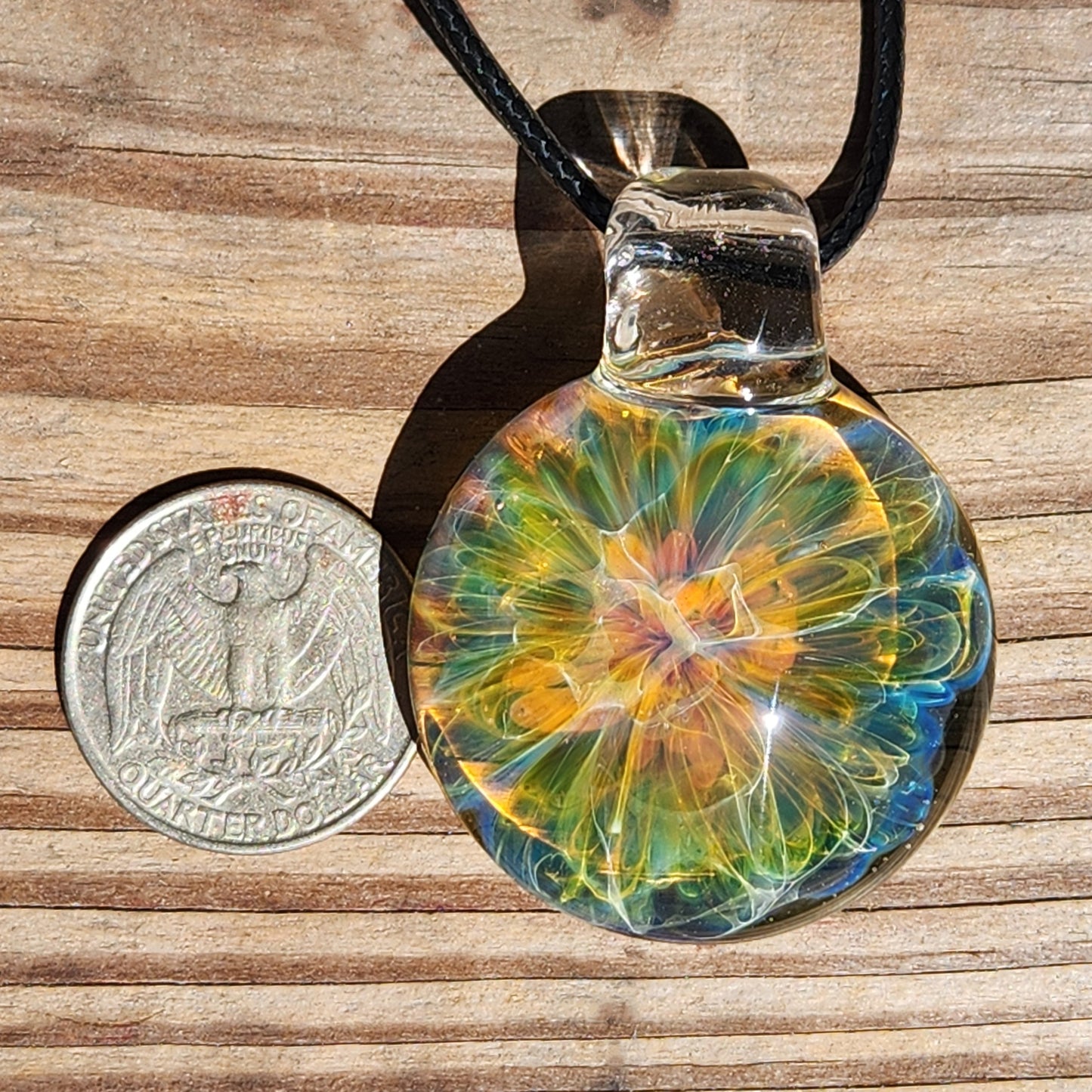 Detailed view of the glass pendant's vibrant multicolor swirl design, with sunlight reflecting off its smooth surface.