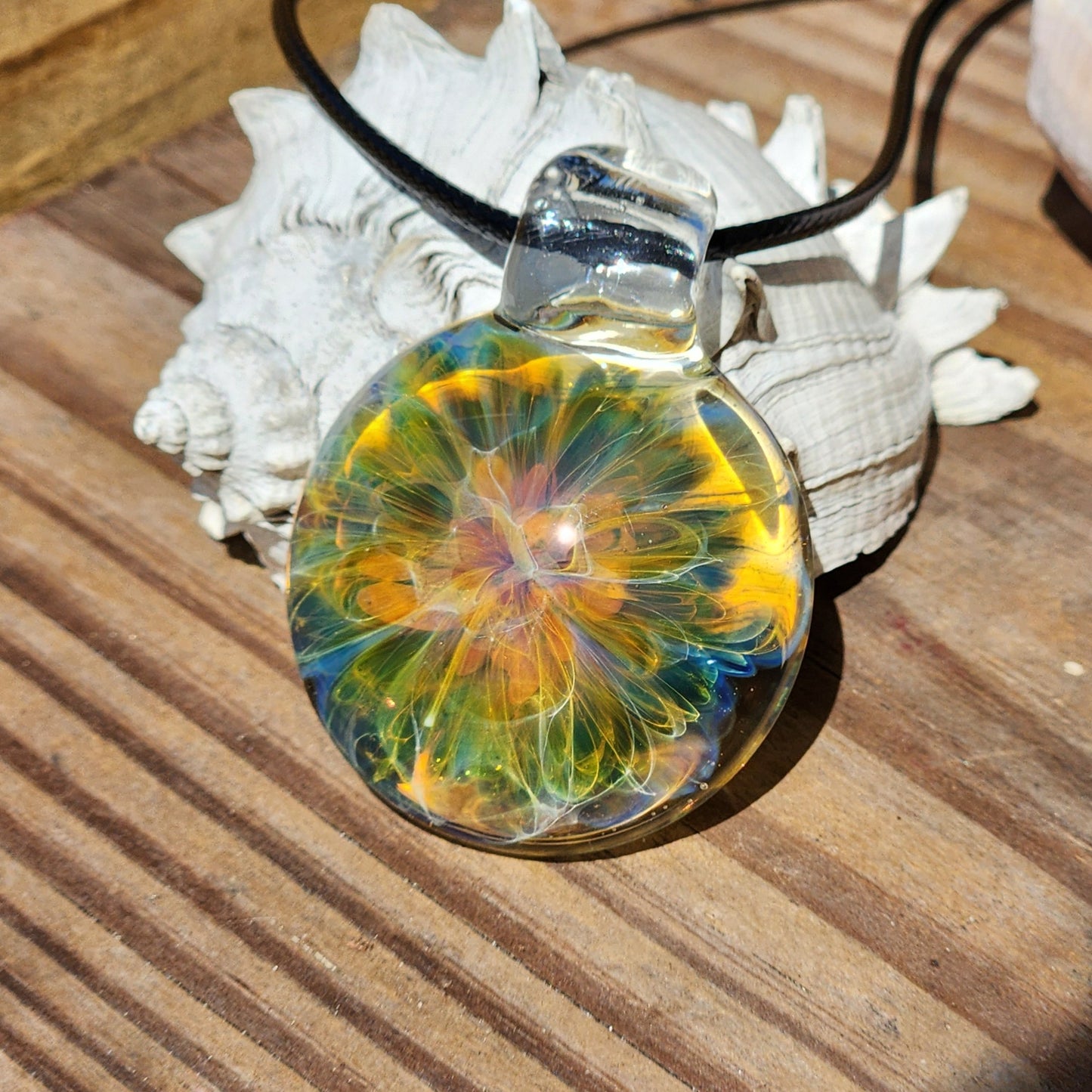 Macro shot of glass pendant with vibrant multicolor swirl, black cord, on white shell, sandy surface