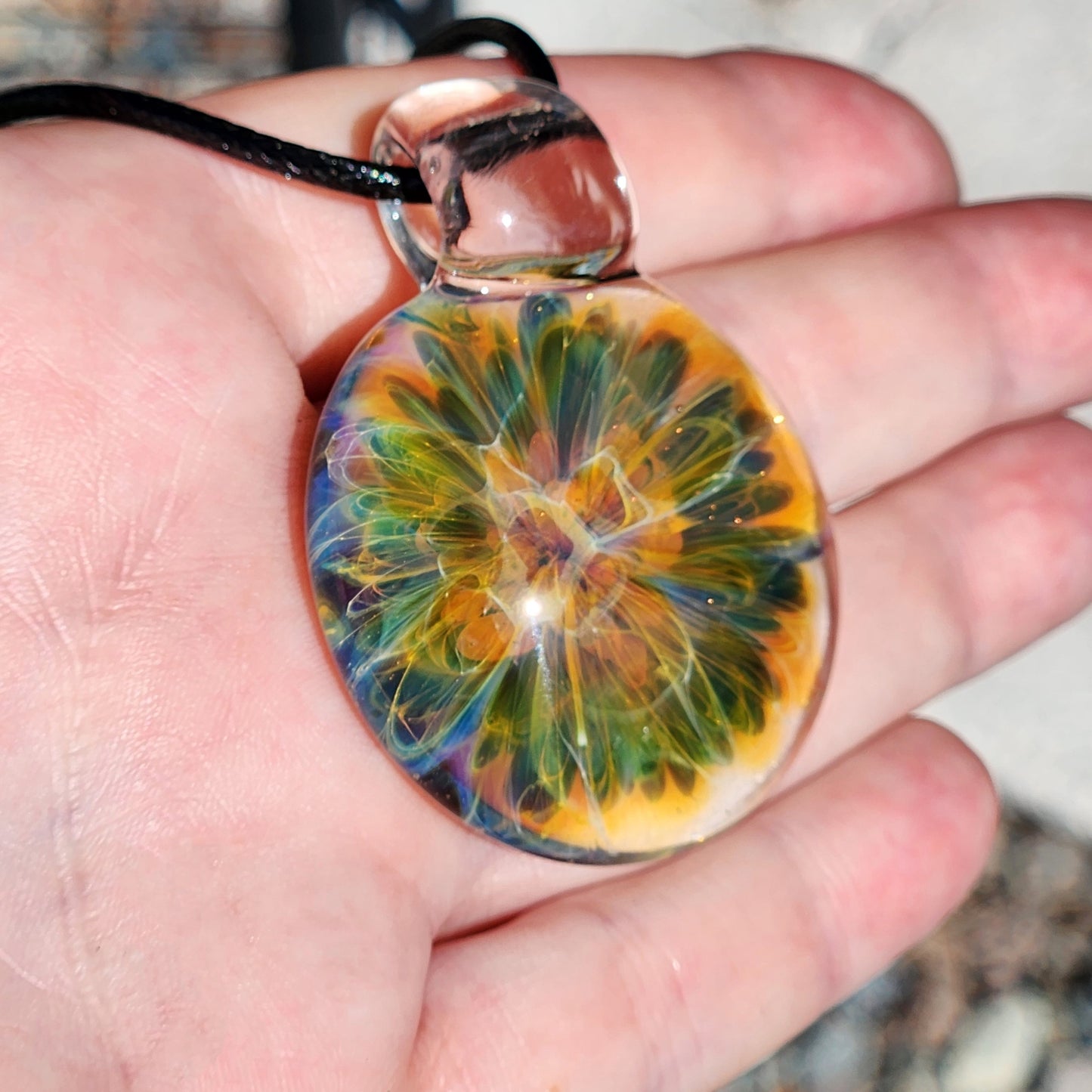 Side angle of the glass pendant necklace highlighting the transparent glass and swirling colors, with a shadow cast on a wooden surface.