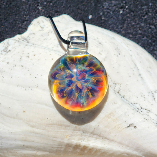 Handmade glass pendant necklace with vibrant rainbow colors, round shape, on black braided cord, displayed on textured white surface
