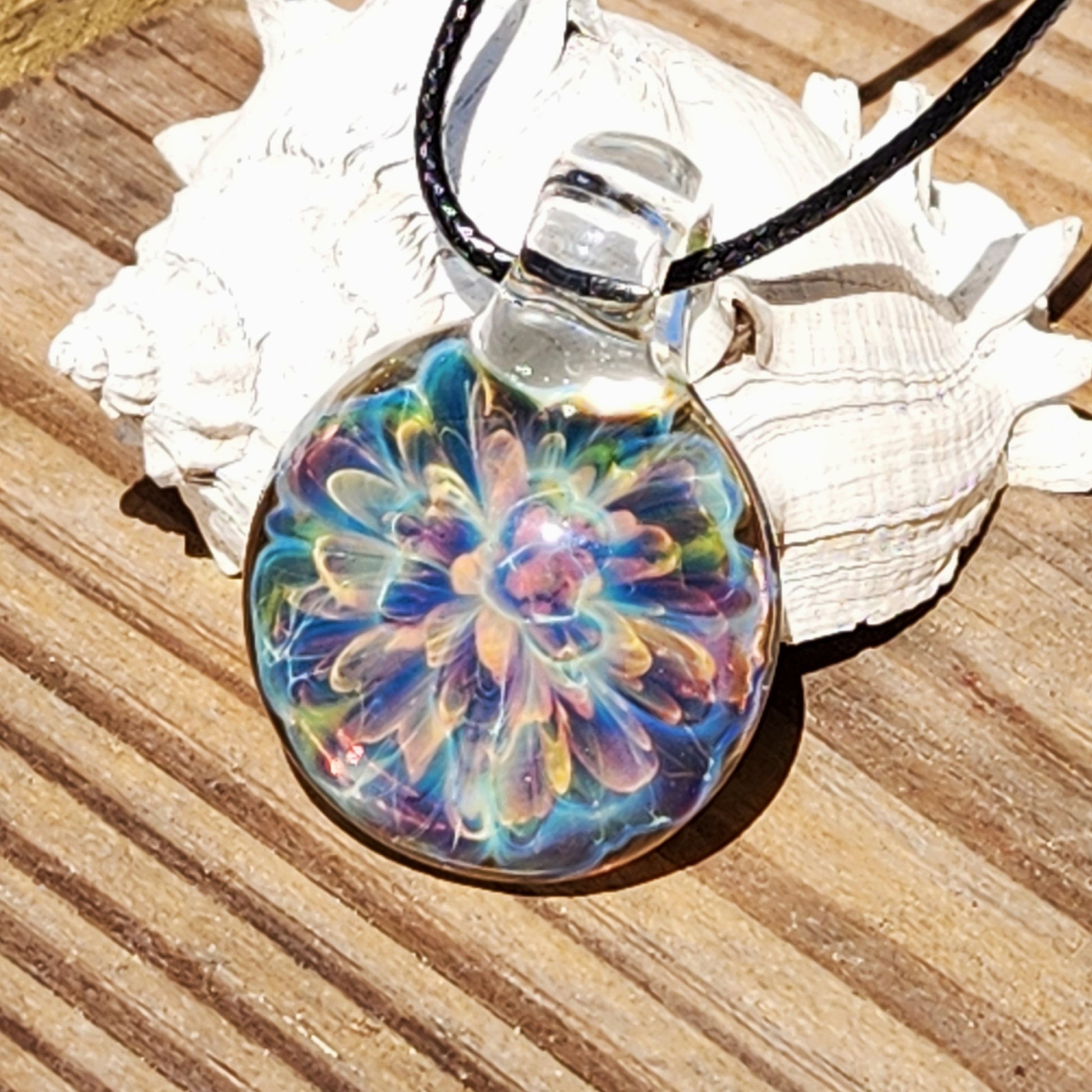 Colorful glass pendant with swirling rainbow design, on black braided cord, on white textured paper background