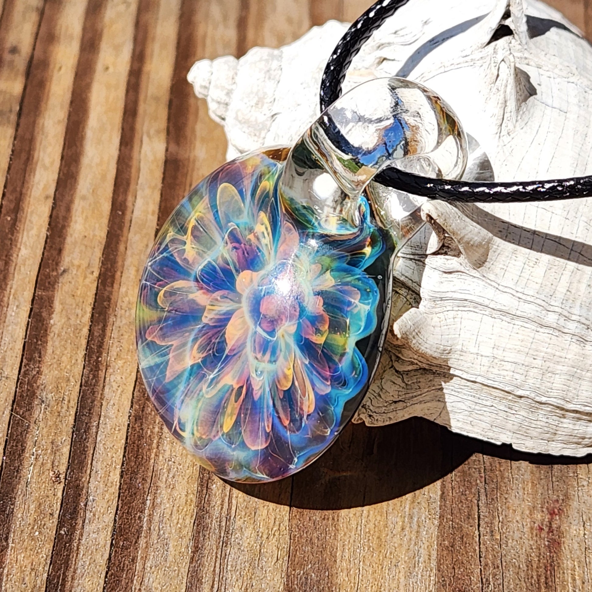 Close-up of colorful glass pendant necklace with rainbow swirl design, hanging on black cord, on wooden surface with white decorative element