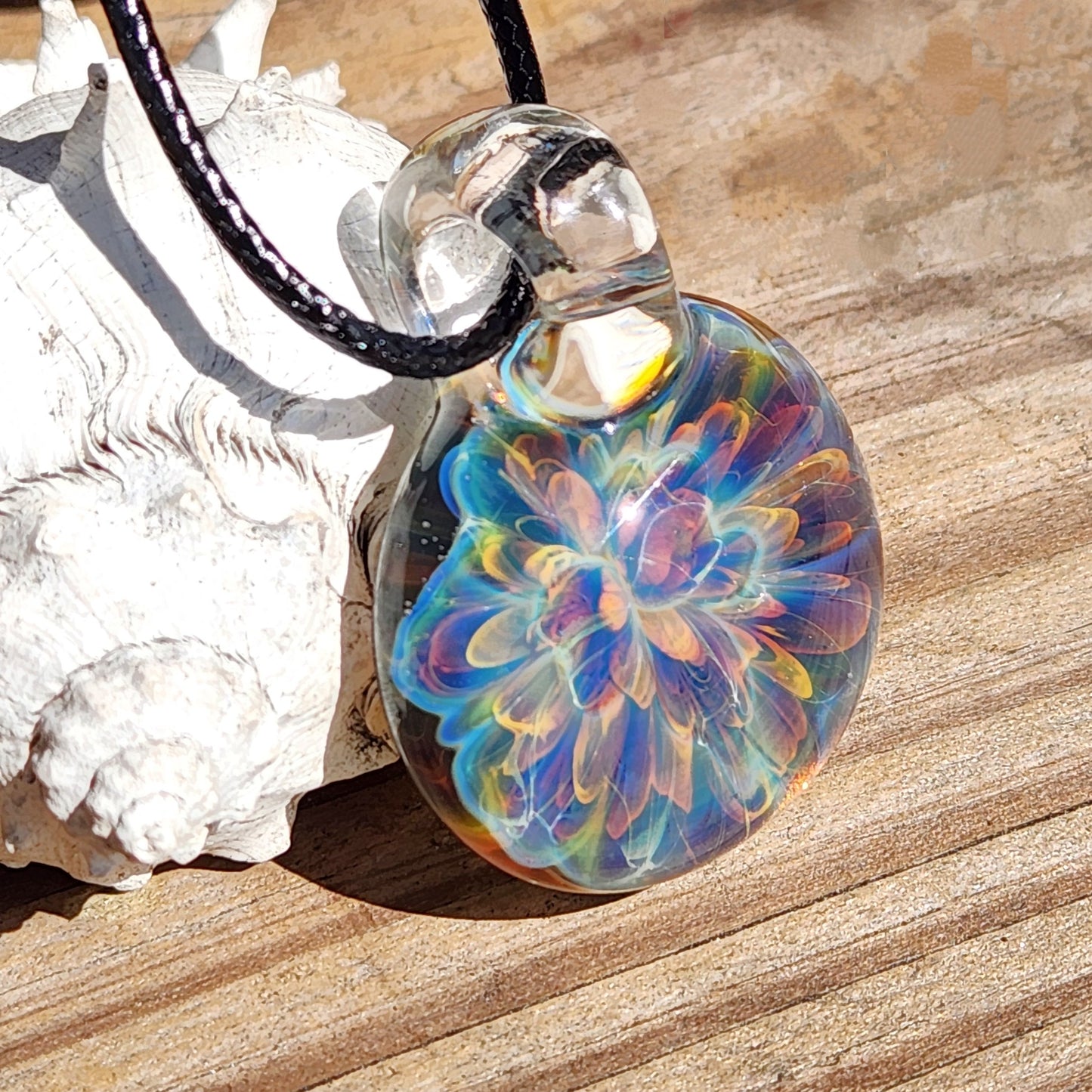 Rainbow swirl glass pendant necklace with teardrop shape, on black braided cord, displayed on wooden surface with white decorative element