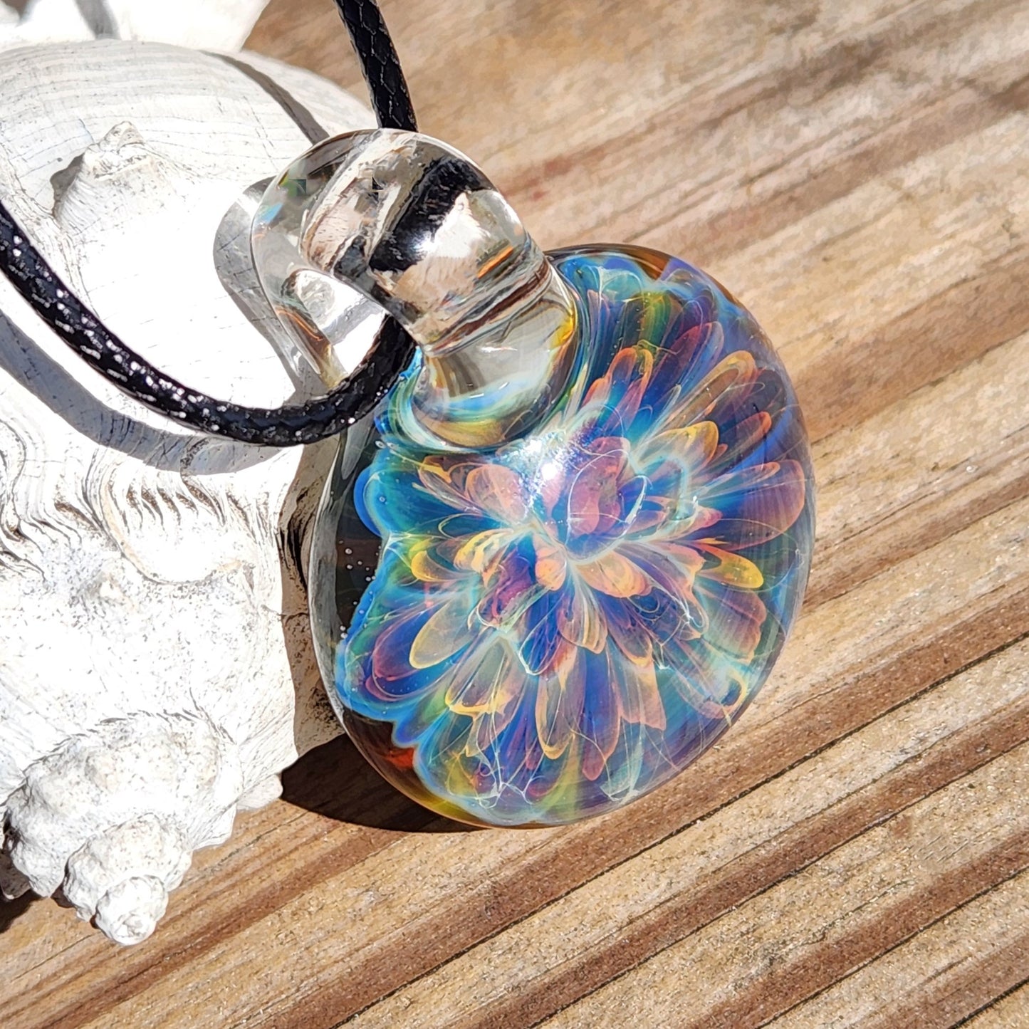 Rainbow swirl glass pendant with vibrant colors, attached to black cord, on white textured paper surface