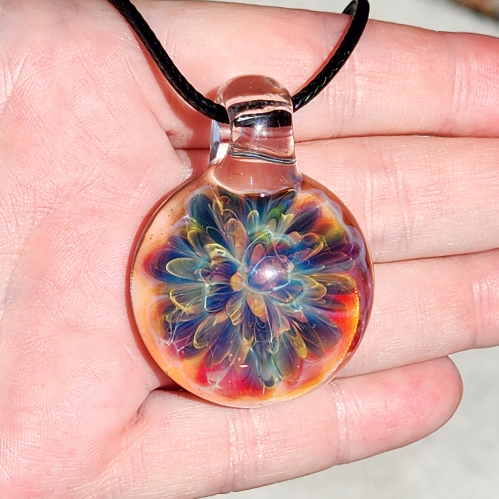 Colorful glass pendant with rainbow swirl design, on black cord, resting on textured white surface, close-up view
