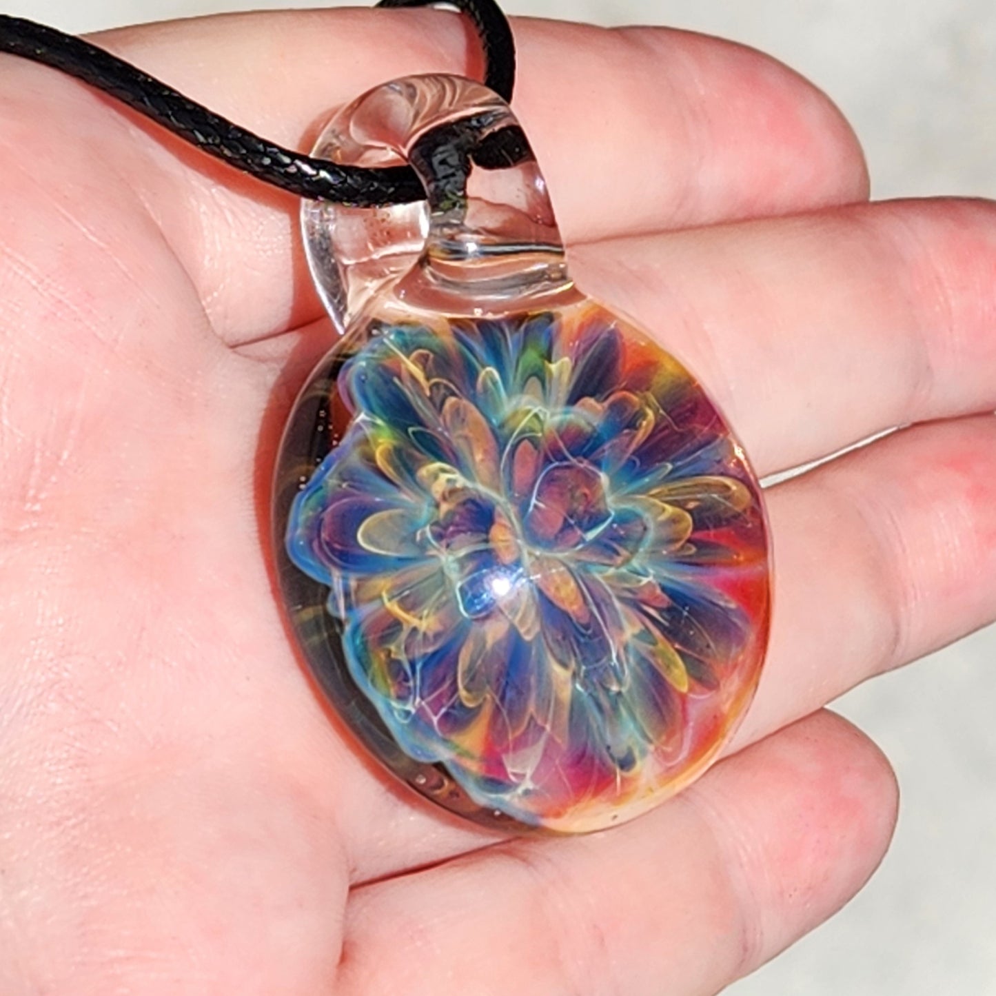 Close-up of rainbow glass pendant with swirling colors, attached to black braided cord, on white textured paper background