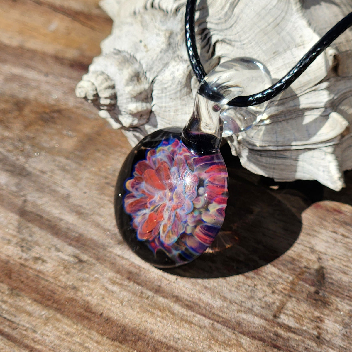 Detailed view of the colorful floral pattern inside the handmade glass pendant, with black cord, on a textured surface.