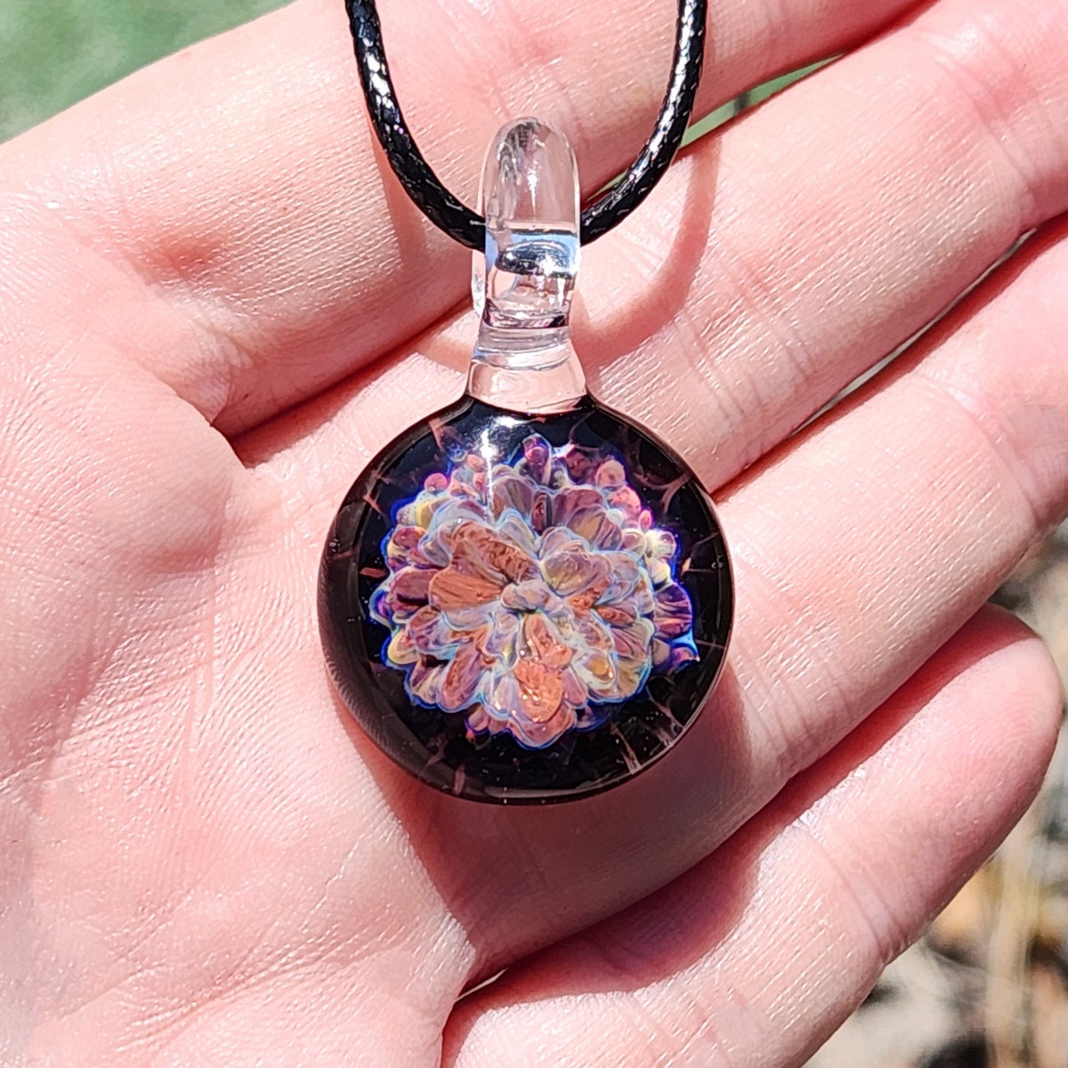 Detailed view of colorful floral glass pendant with black cord, showcasing intricate design and craftsmanship
