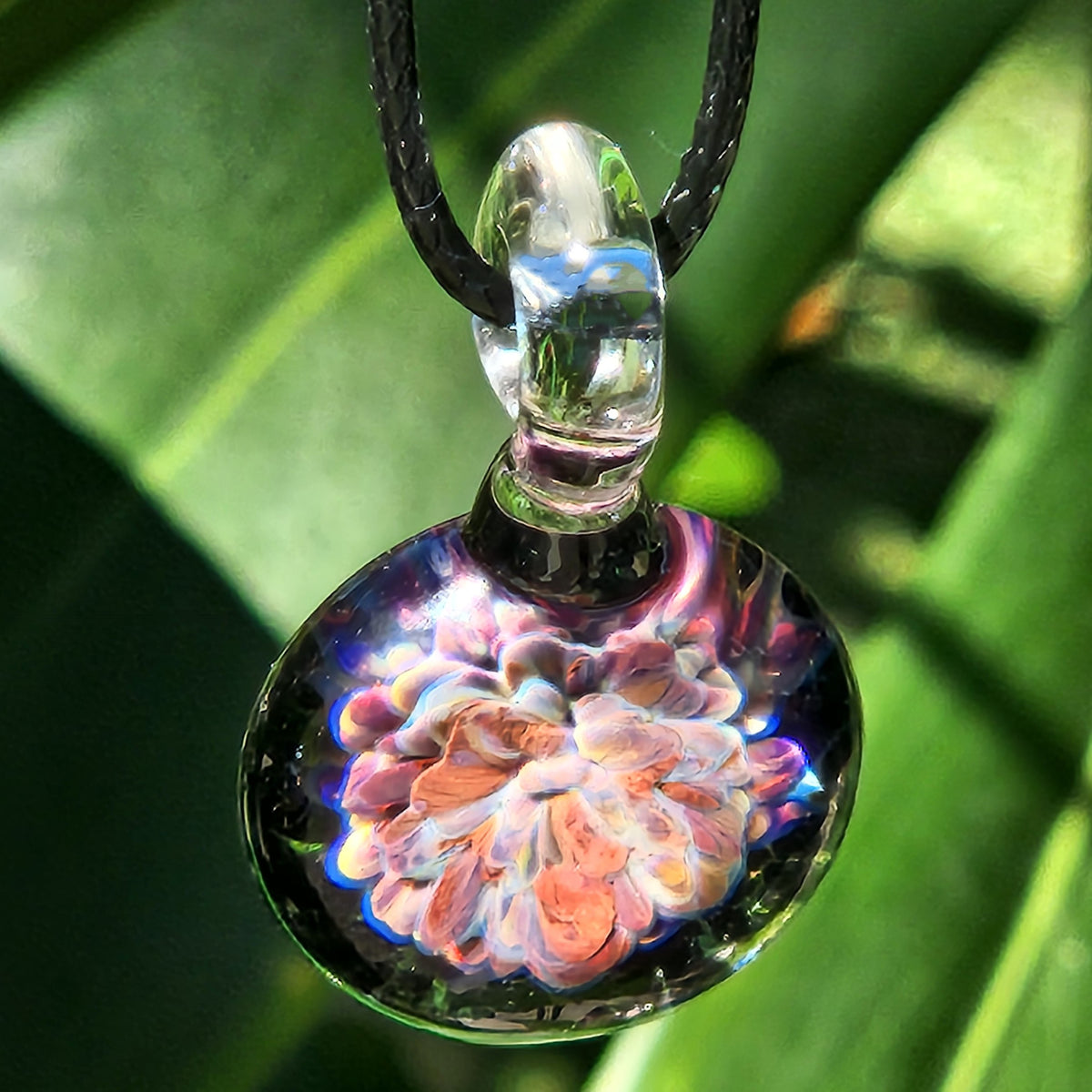 Close-up of a handmade glass pendant with vibrant floral design, transparent glass, small size, ideal for jewelry and gifts