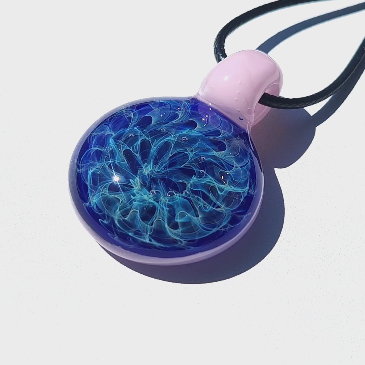Heady glass pendant necklace featuring a vibrant blue core with silver and gold fuming, encased in a soft pink loop on a black cord.