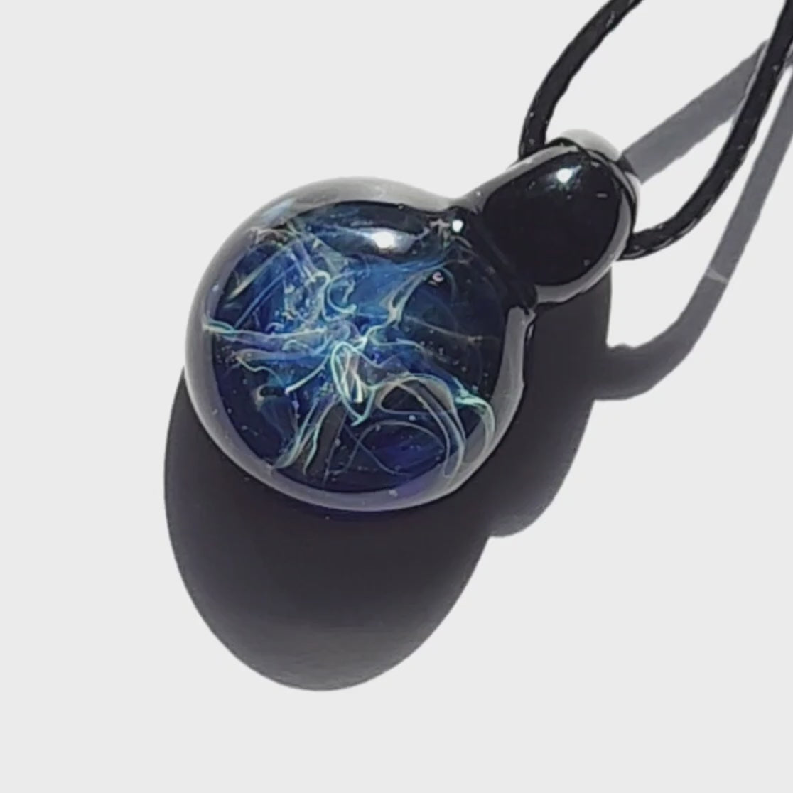 Small blue swirl glass pendant necklace casting a shadow, showcasing its glossy handmade finish and intricate design.