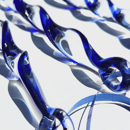 Blue holiday suncatcher ornaments in sunlight highlighting the clear and cobalt glass twist. Unique handmade Christmas décor for home or garden.
