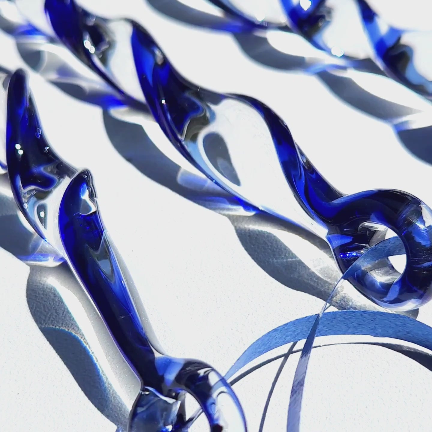 Blue holiday suncatcher ornaments in sunlight highlighting the clear and cobalt glass twist. Unique handmade Christmas décor for home or garden.