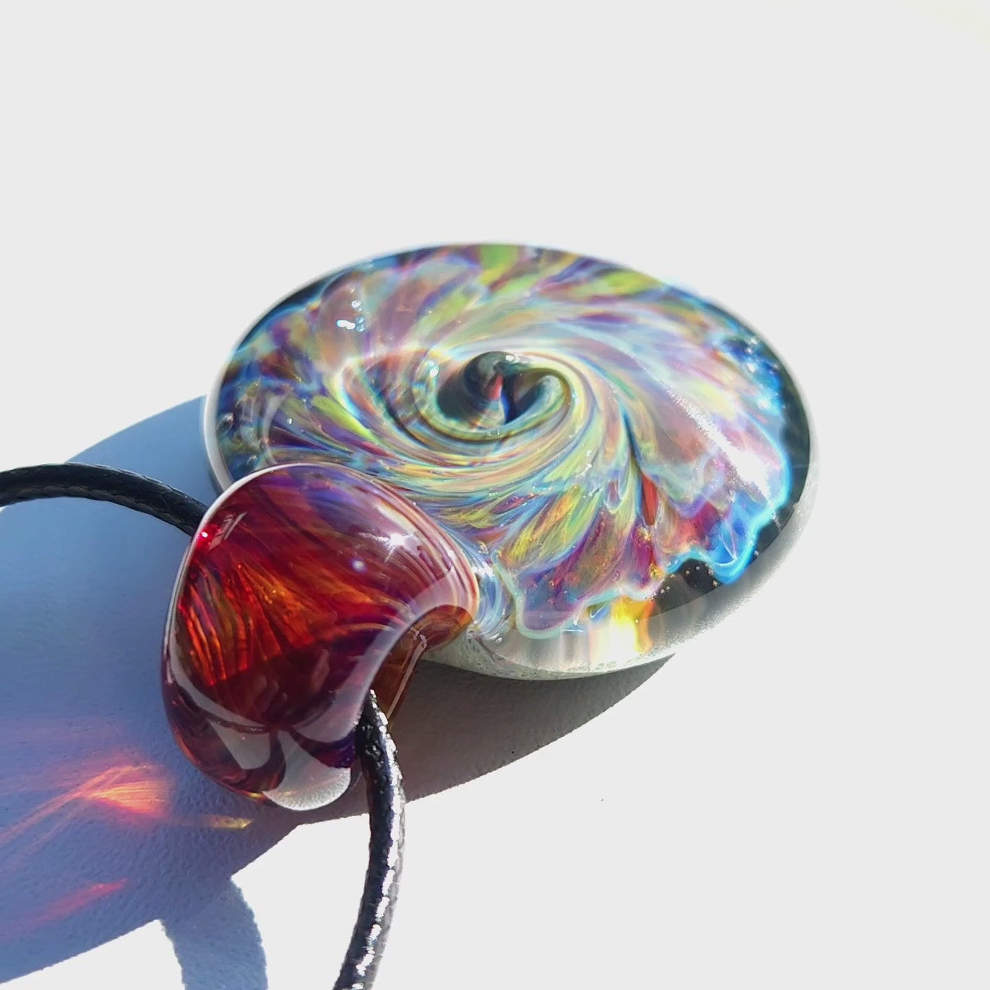 Close-up of multicolor glass pendant necklace showing iridescent swirl and red-amber loop, handmade artisan jewelry.