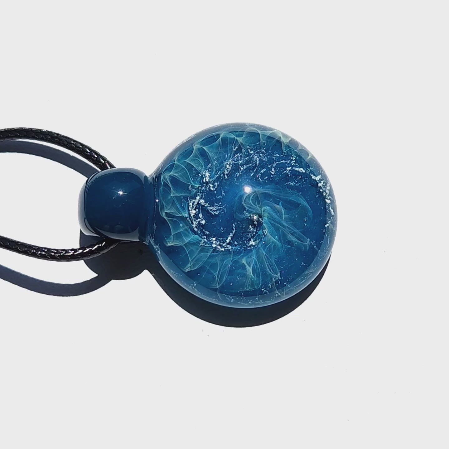 Swirling wave design in a handmade blown glass pendant necklace, highlighted under direct sunlight on a white background.