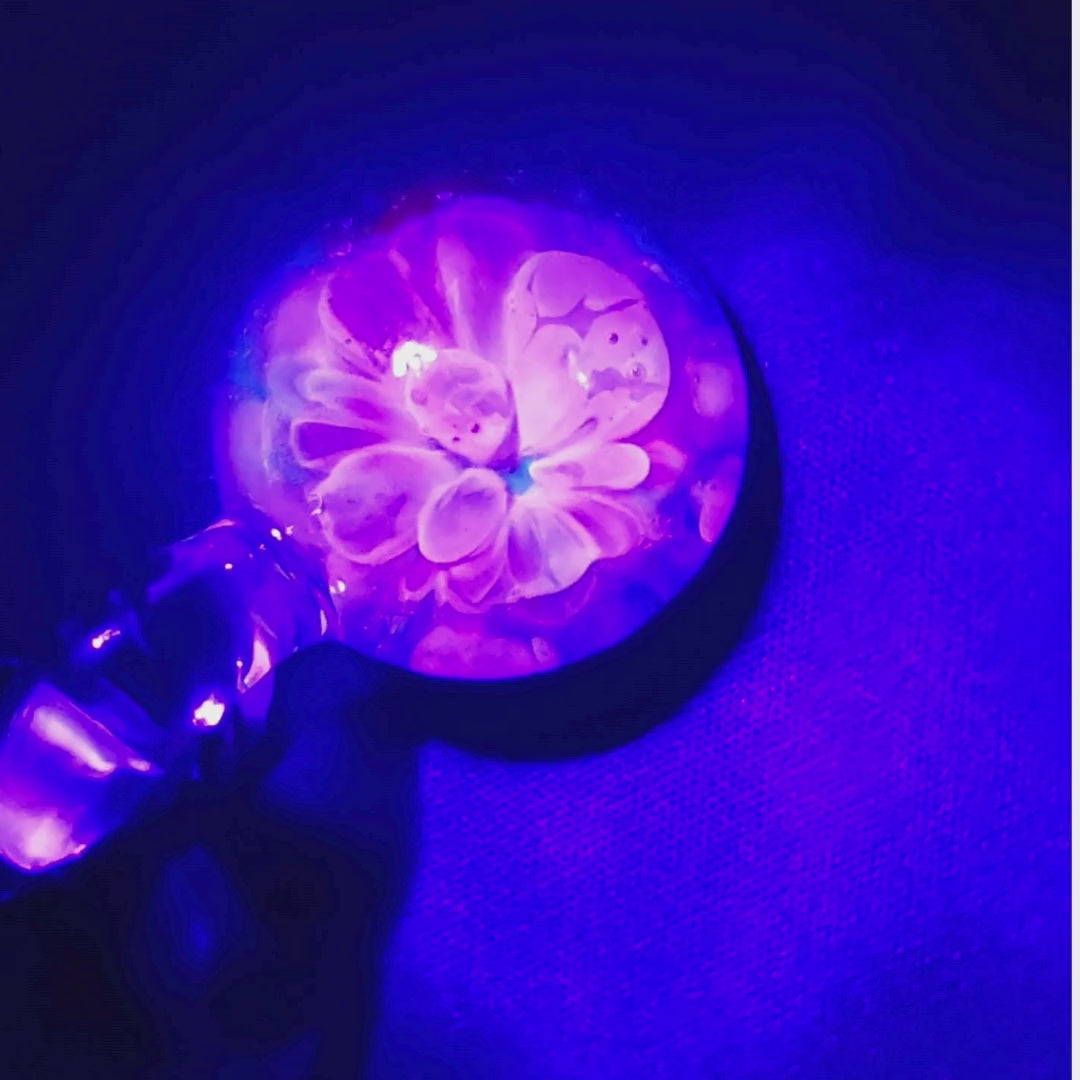 Close-up of Handmade Glass Pendant under UV light, revealing a glowing pink and purple floral bloom effect.
