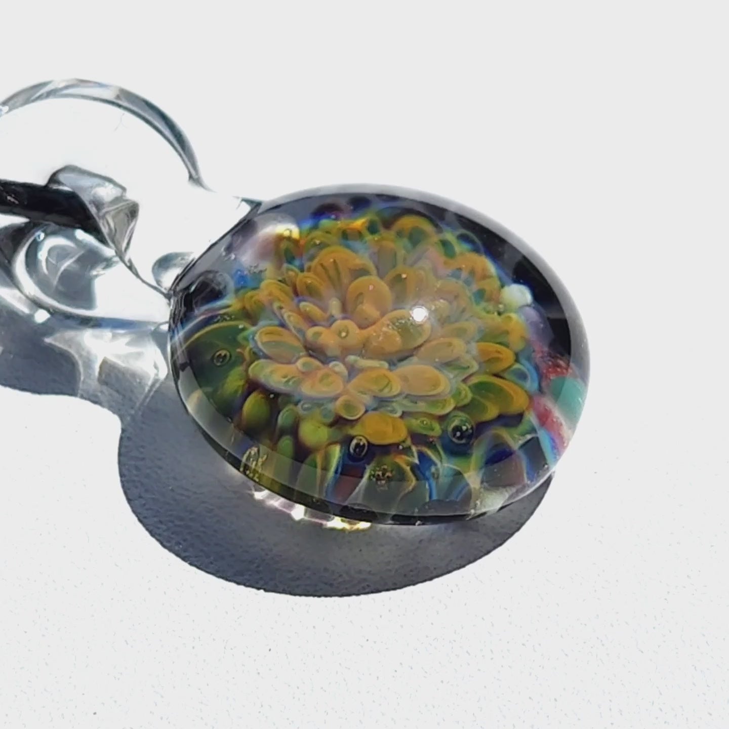 Close-up of handmade glass pendant showcasing detailed yellow and green flower encased in clear glass, part of unique jewelry collection.