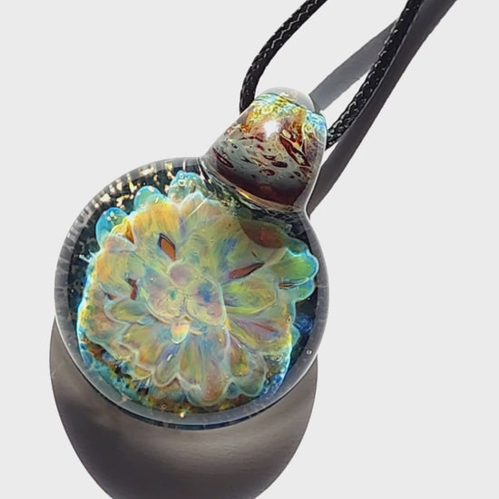 Handmade glass pendant necklace with a glowing yellow and blue flower encased in clear glass, suspended on a black cord.