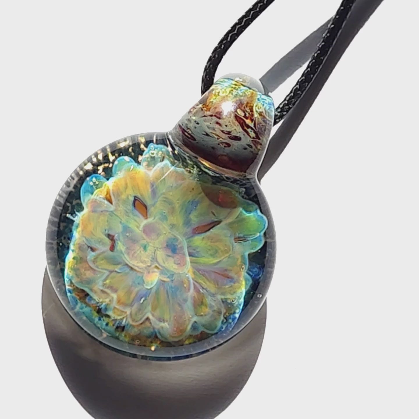 Handmade glass pendant necklace with a glowing yellow and blue flower encased in clear glass, suspended on a black cord.