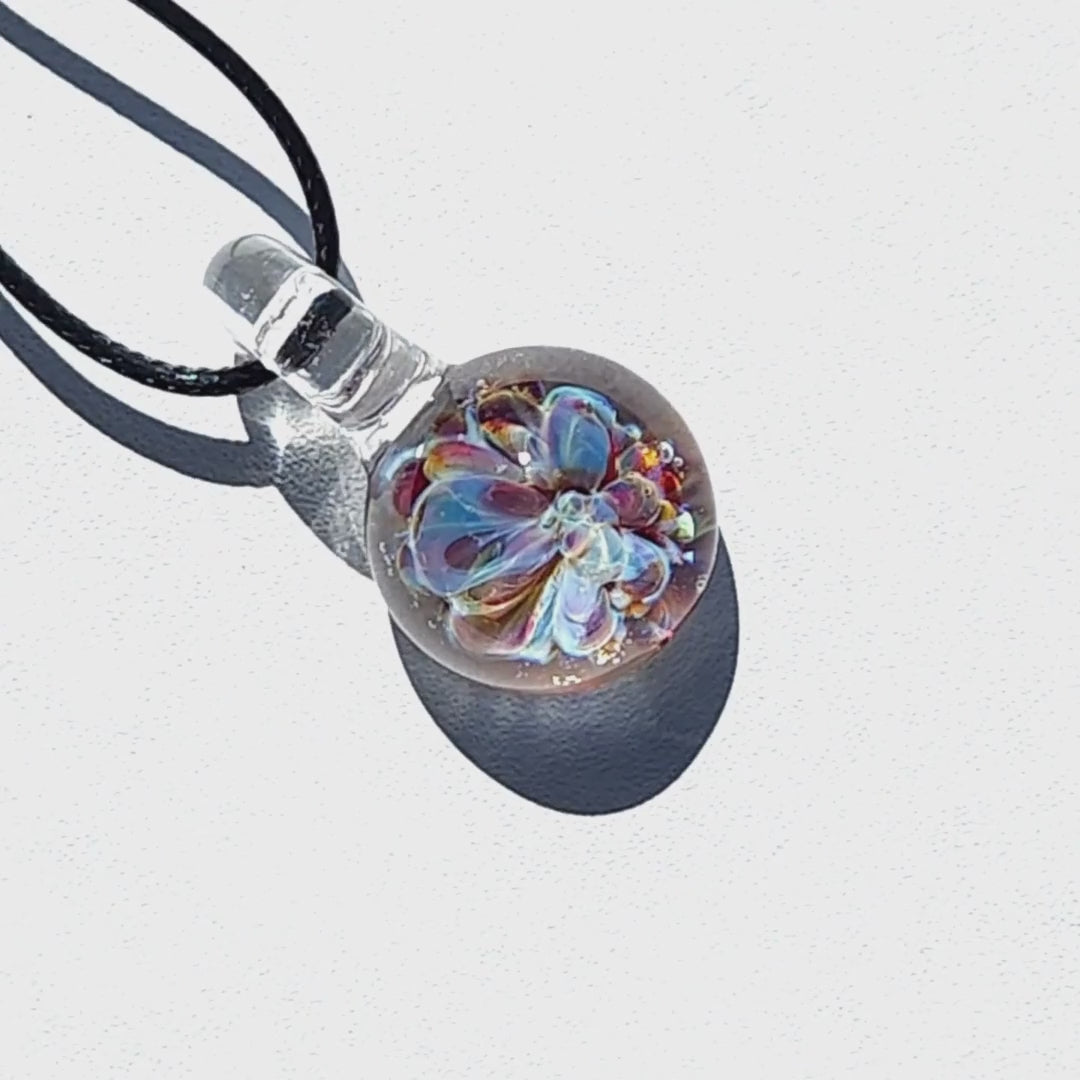 UV Glow Glass Pendant casting a shadow on white background, highlighting the intricate flower design. Handmade blown glass necklace for accessories.