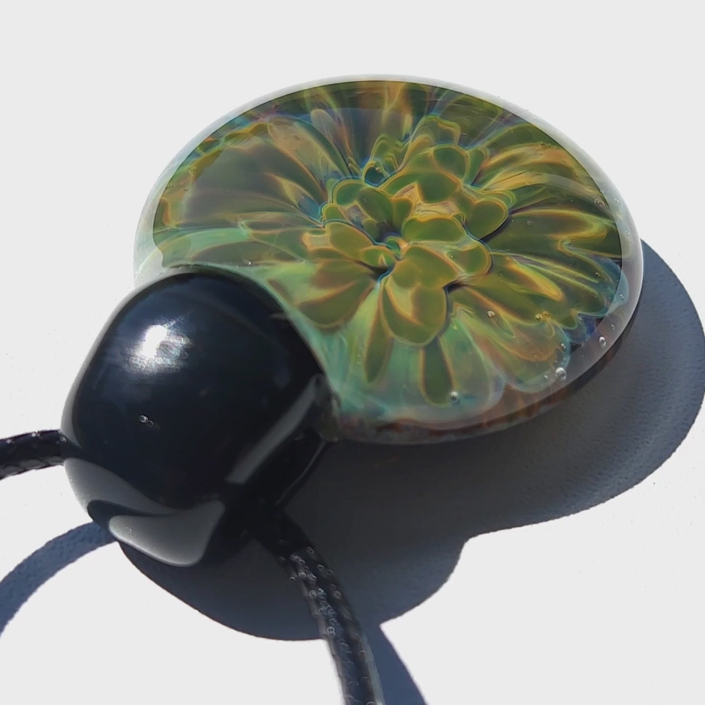 Handmade glass pendant featuring a glowing yellow-green flower design, shown under bright light. Part of handmade jewelry collection.